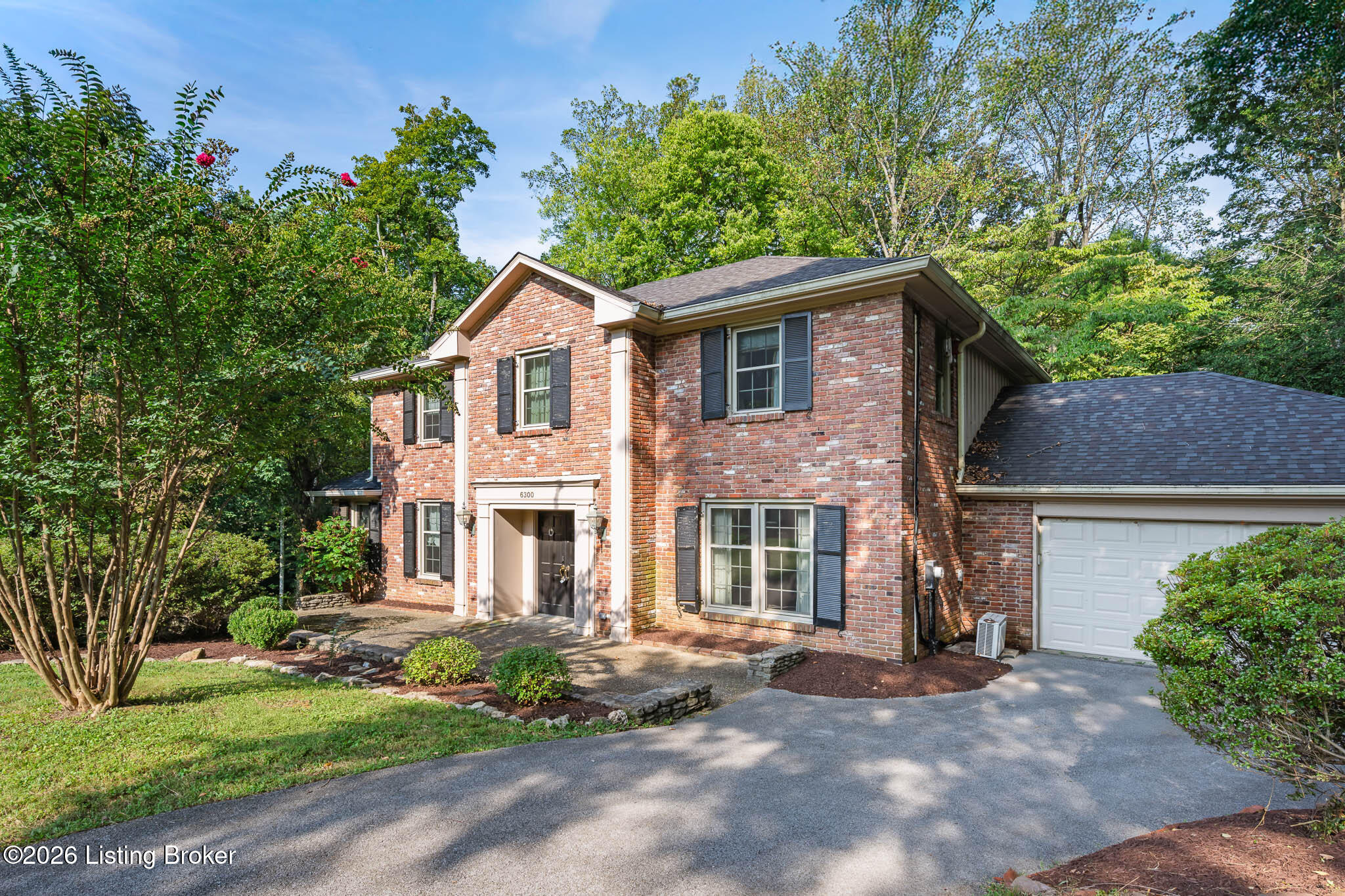 Two-story brick house with dark shutters, attached garage, and landscaped front yard.