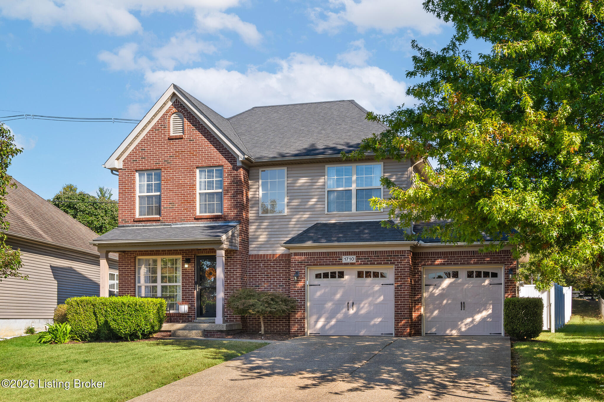 Two-story brick and gray-sided house with a double garage, broad driveway, and leafy tree.
