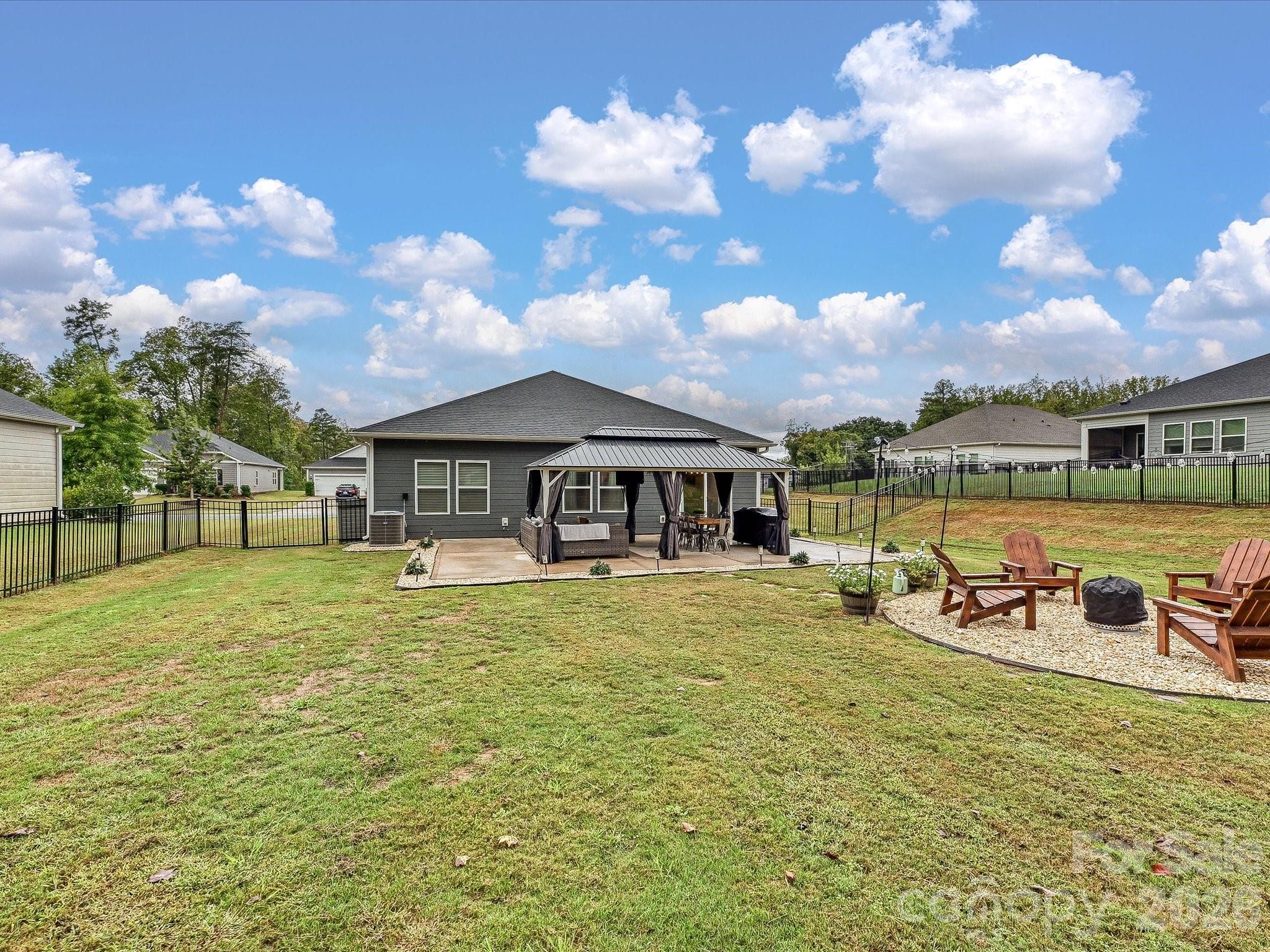 House with a covered patio, fenced lawn, and gravel fire-pit seating area.
