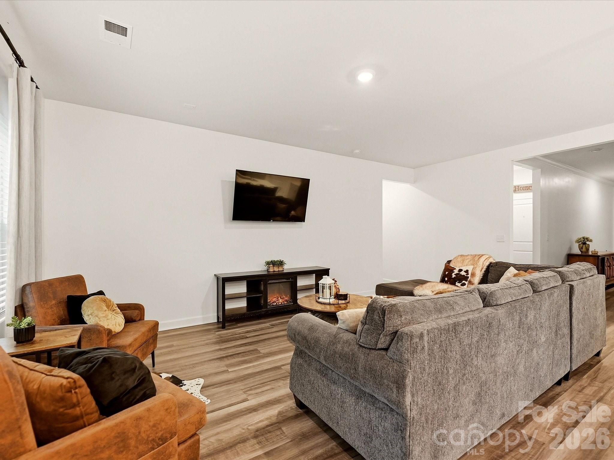 Staged living room with gray sectional, rust-colored chairs, and wall-mounted TV above an electric fireplace.