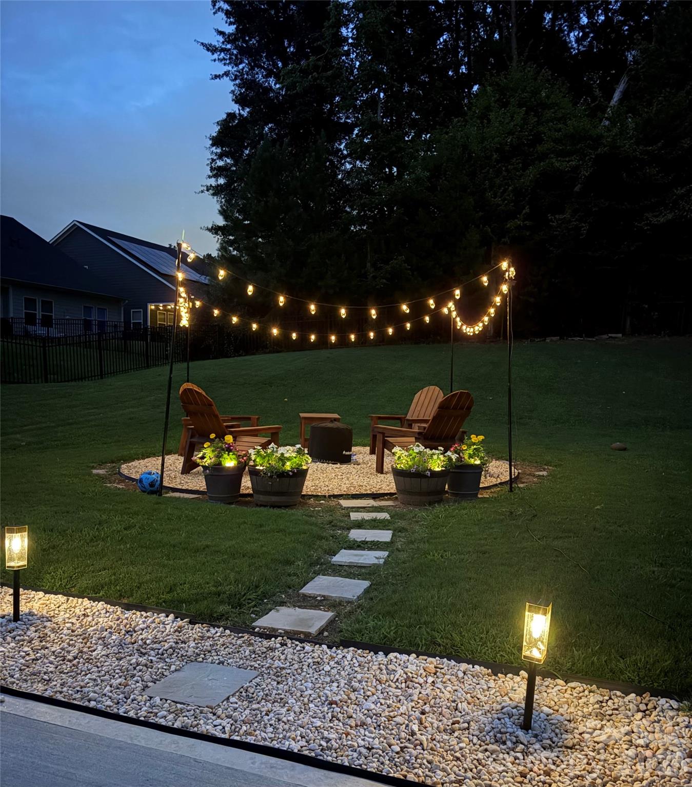 Backyard gravel patio with Adirondack chairs, a fire pit, and glowing string lights.