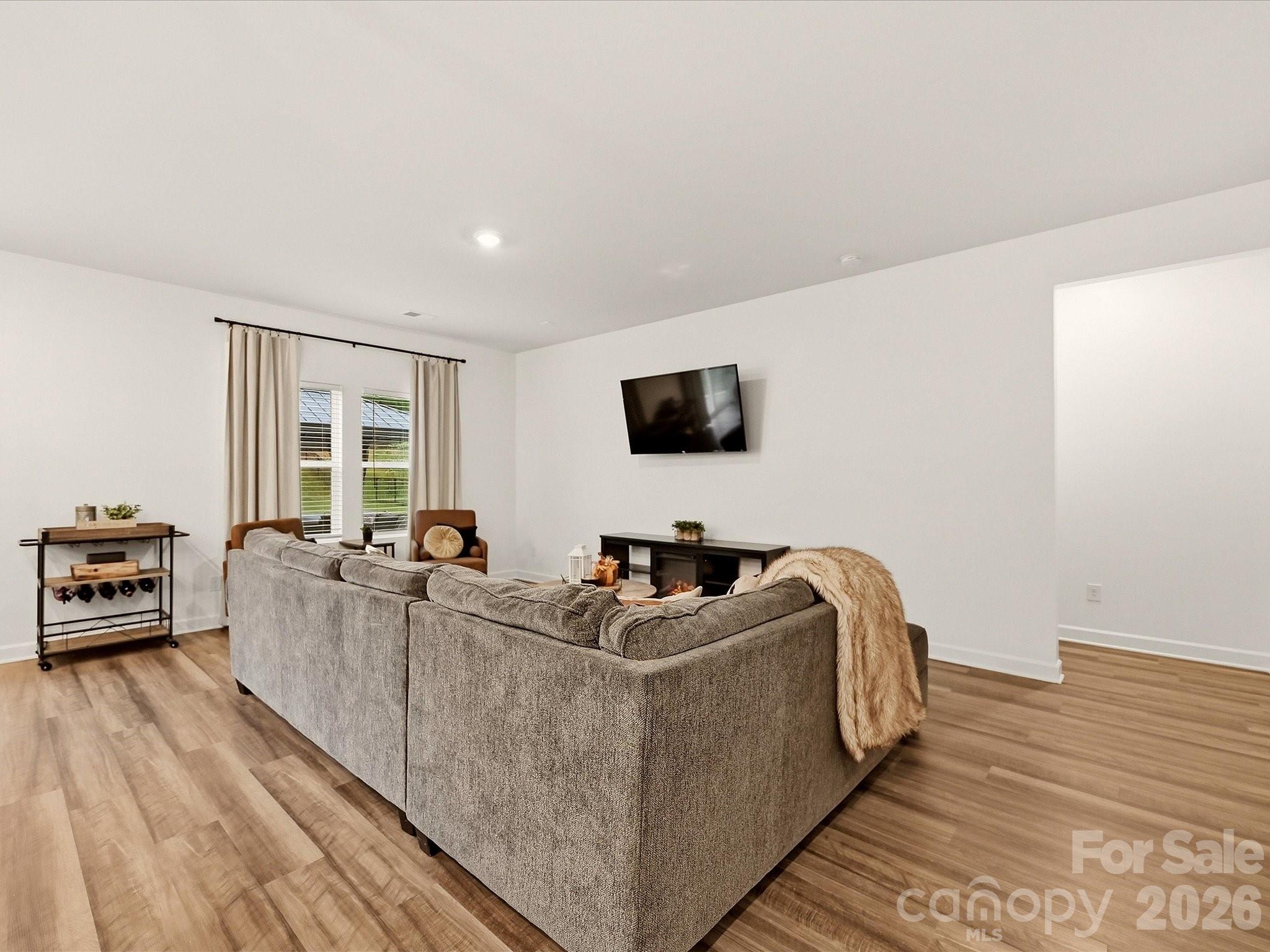 Staged living room with a gray sectional, wood-look floors, and a wall-mounted television.