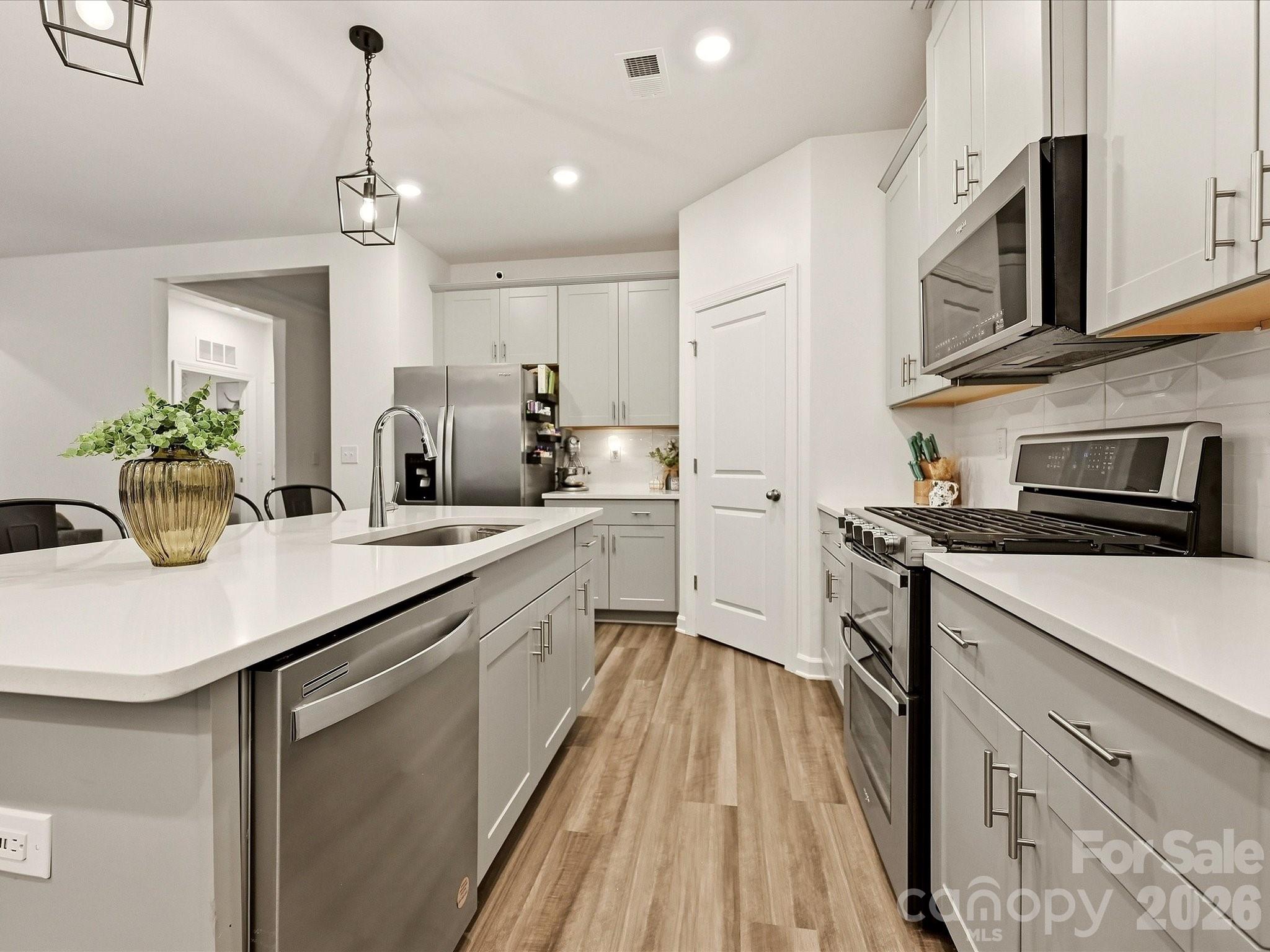 Modern kitchen with white cabinetry, a quartz island, stainless steel appliances, and wood-look flooring.