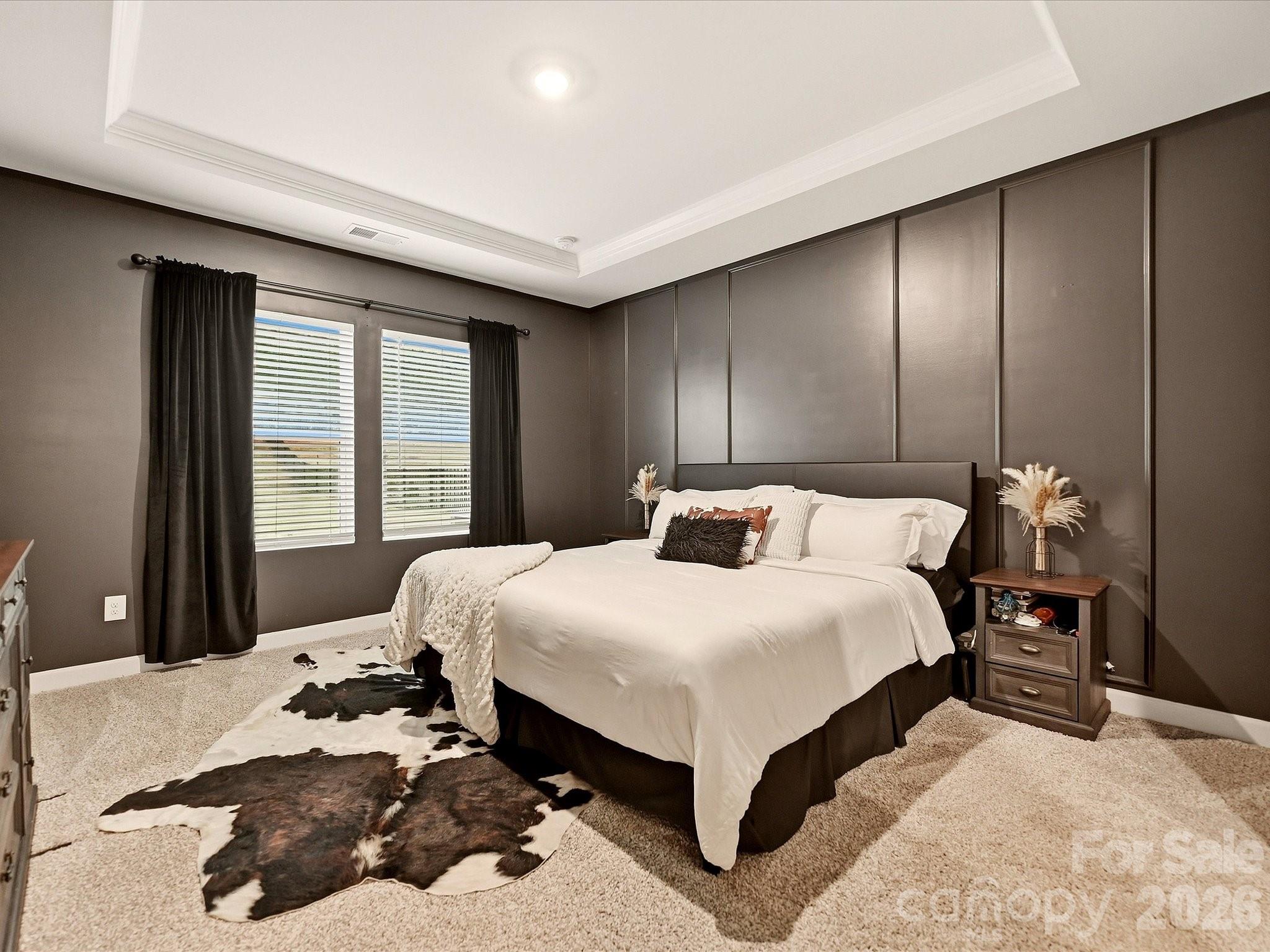Staged bedroom with a white bed, dark paneled wall, and cowhide rug.