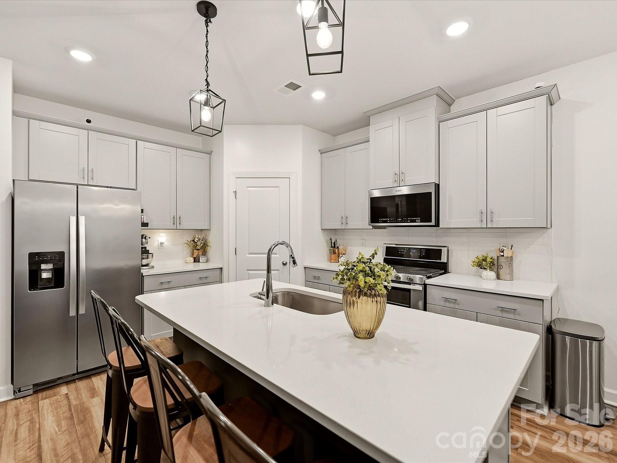 Modern kitchen with a large white island, stainless steel appliances, and white shaker cabinets.