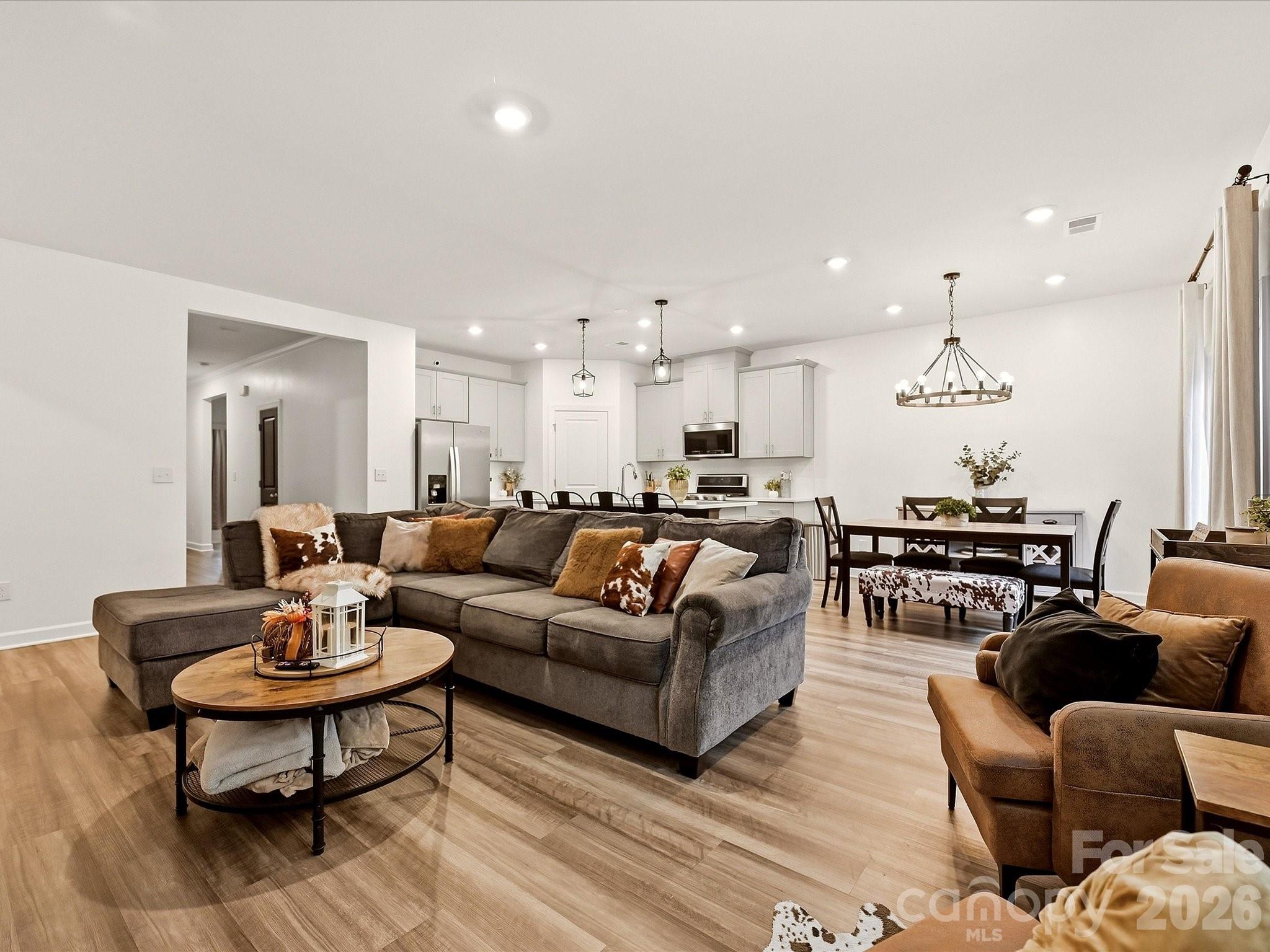 Open-plan living room with gray sectional, dining area, and white kitchen beyond.