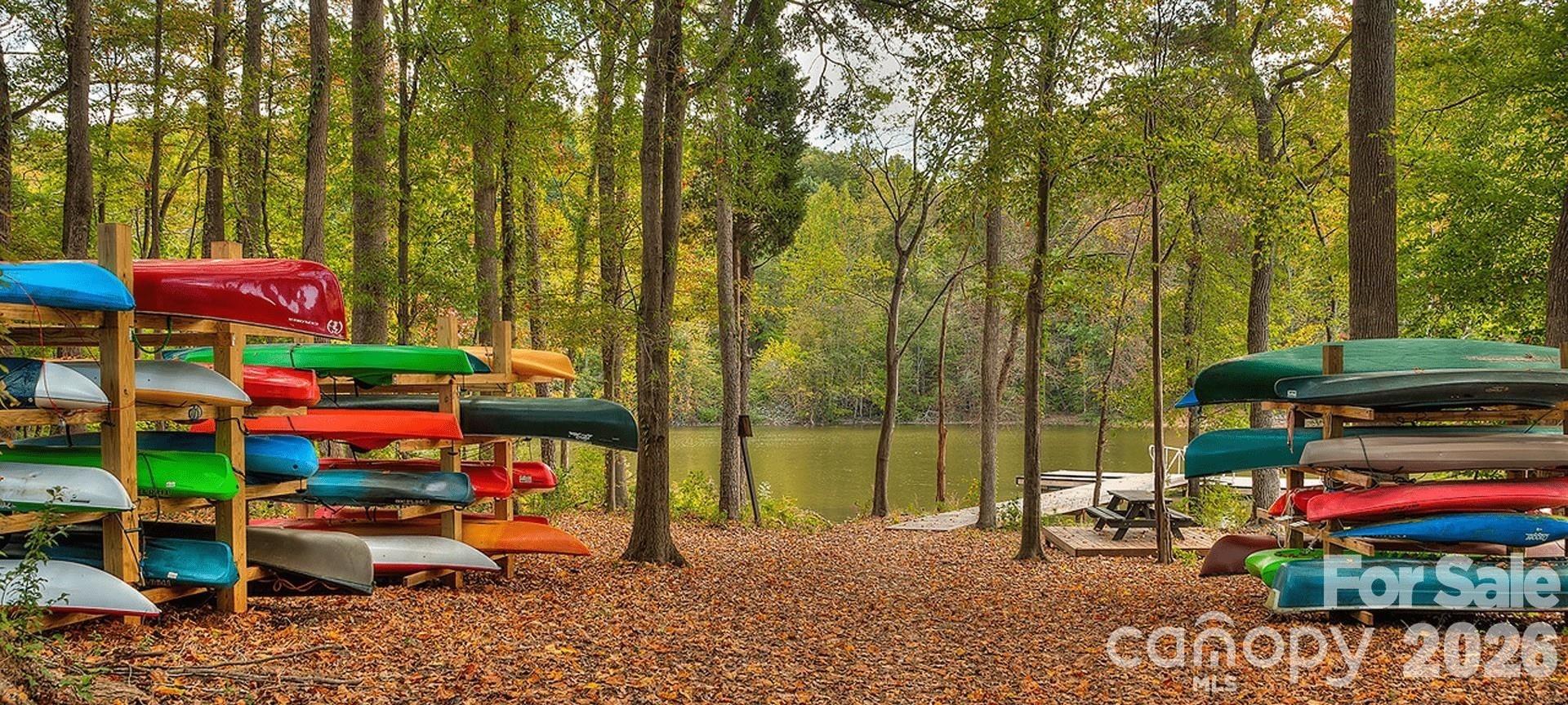Kayaks beside a wooded lake, with a small dock and picnic table along the autumn shoreline.