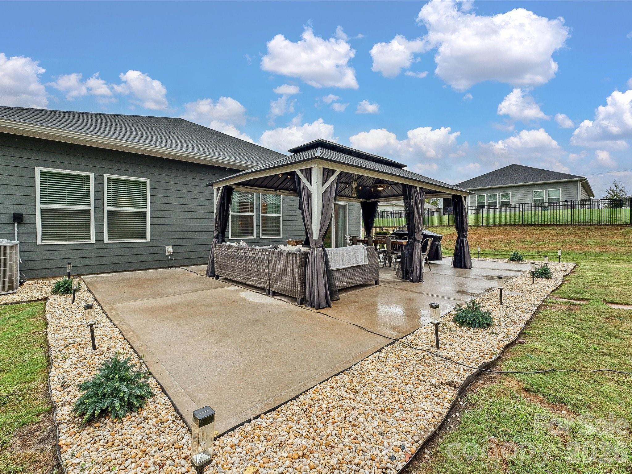 Backyard patio with a curtained pergola, wicker seating, dining set, and stone landscaping.