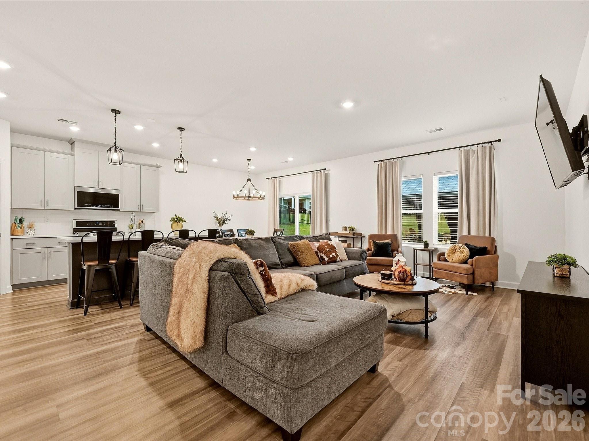 Open-plan living room and kitchen with a gray sectional, island seating, and tall curtained windows.