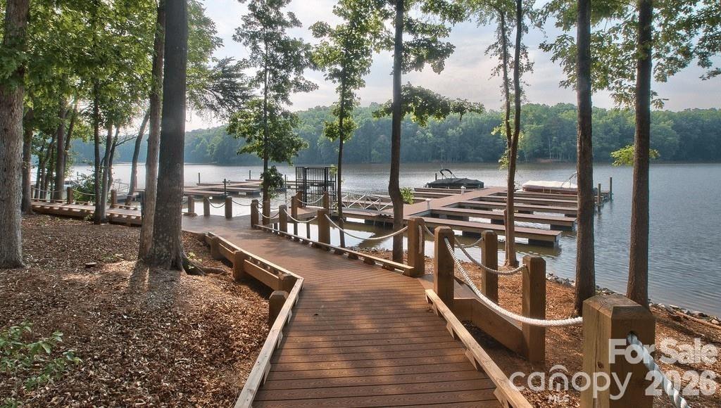 Wooden boardwalk leads through trees to boat docks on a calm lake.