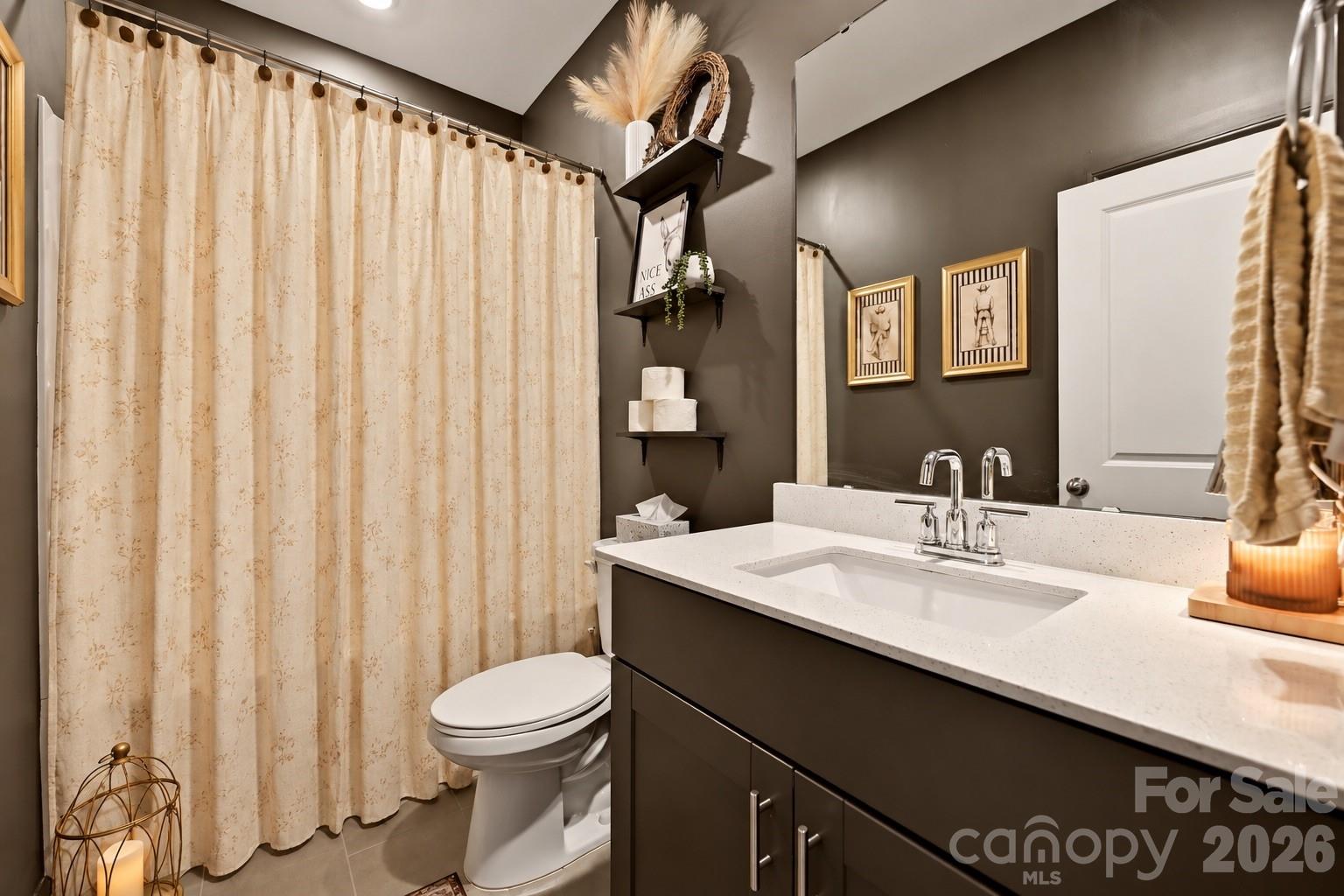 Bathroom with a dark vanity, white sink, toilet, and beige patterned shower curtain.