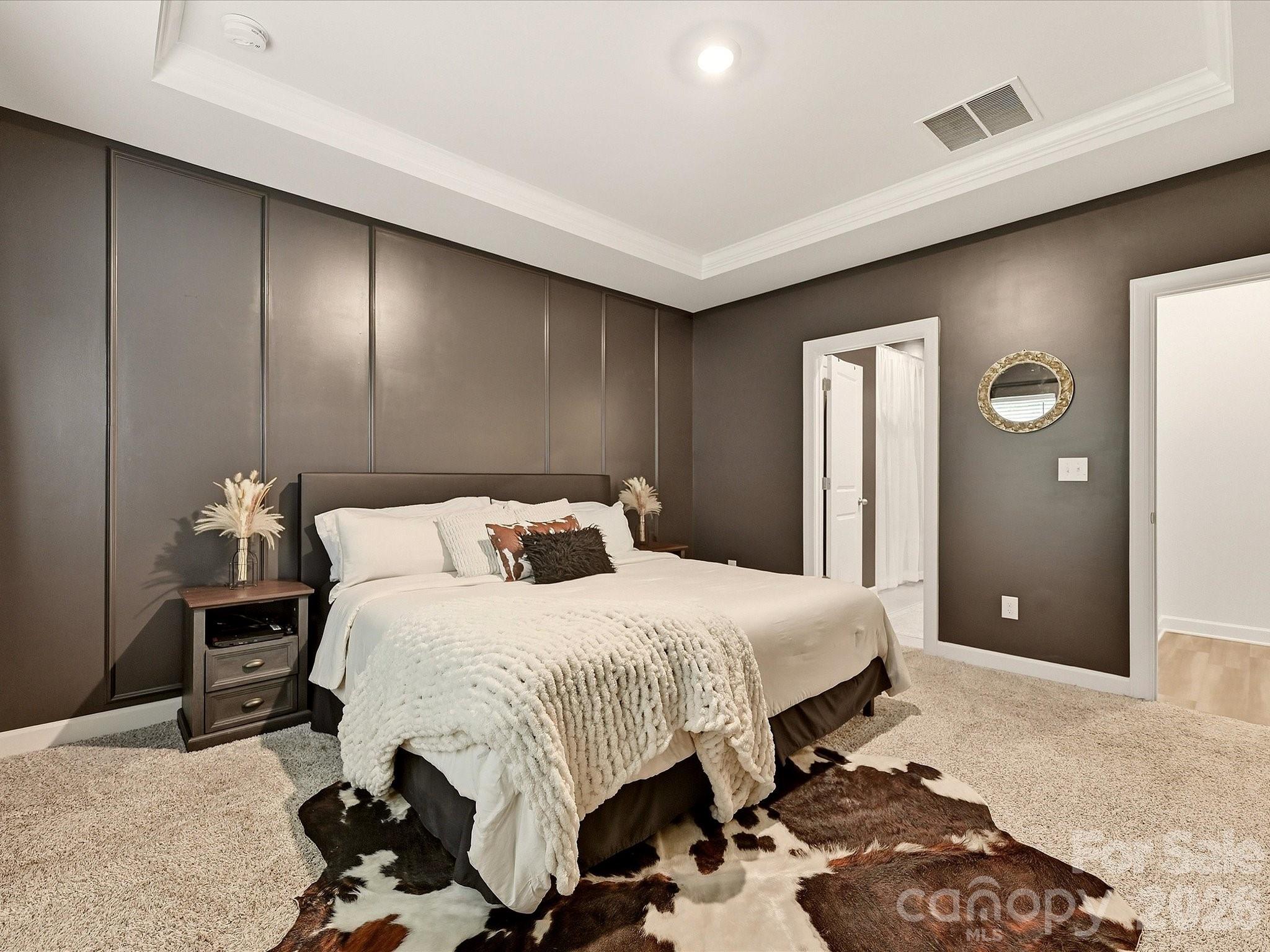 Furnished bedroom with a large white bed, dark paneled wall, and cowhide rug.