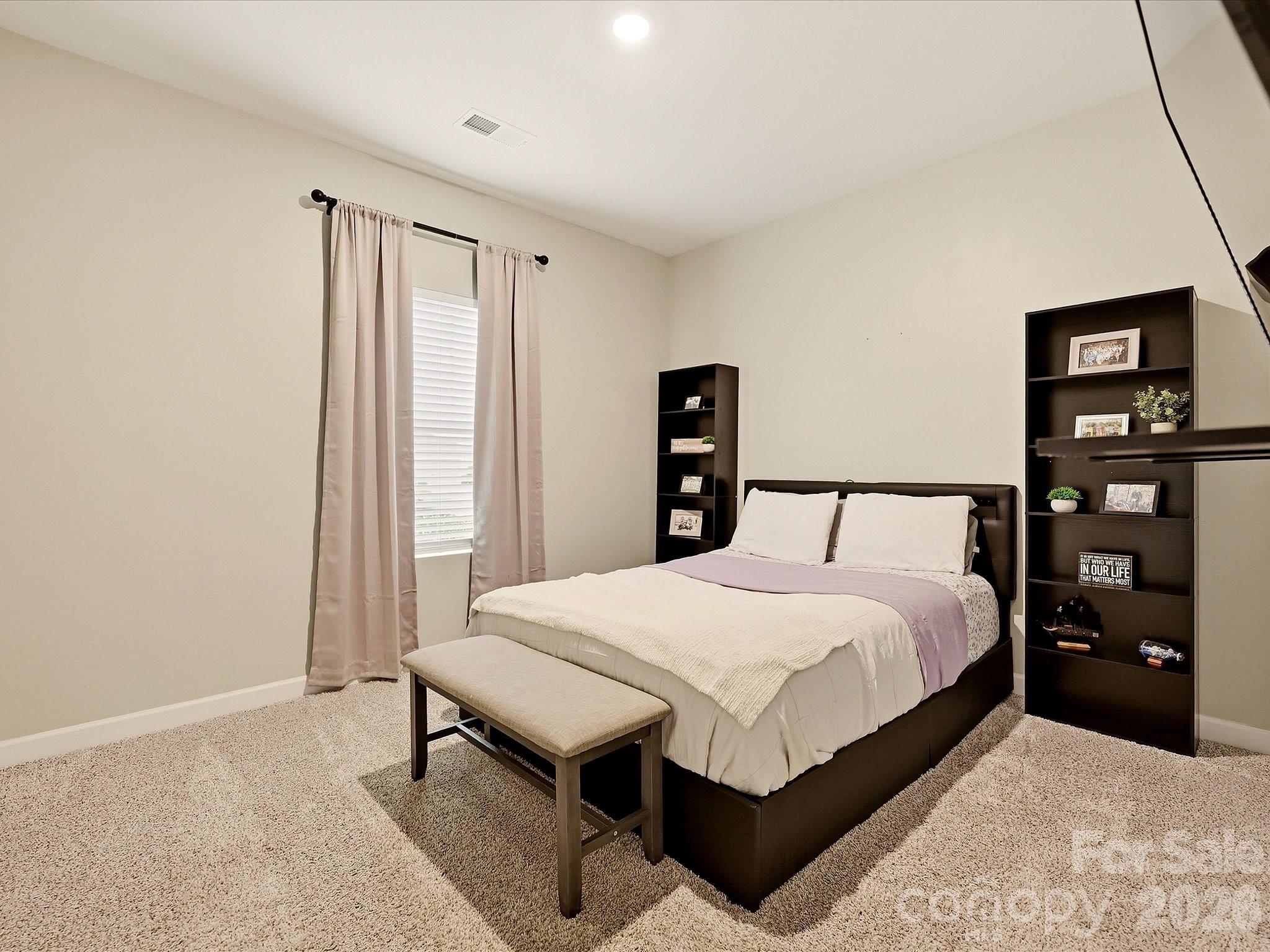Furnished bedroom with a dark platform bed, lavender throw, footboard bench, and tall dark shelves.