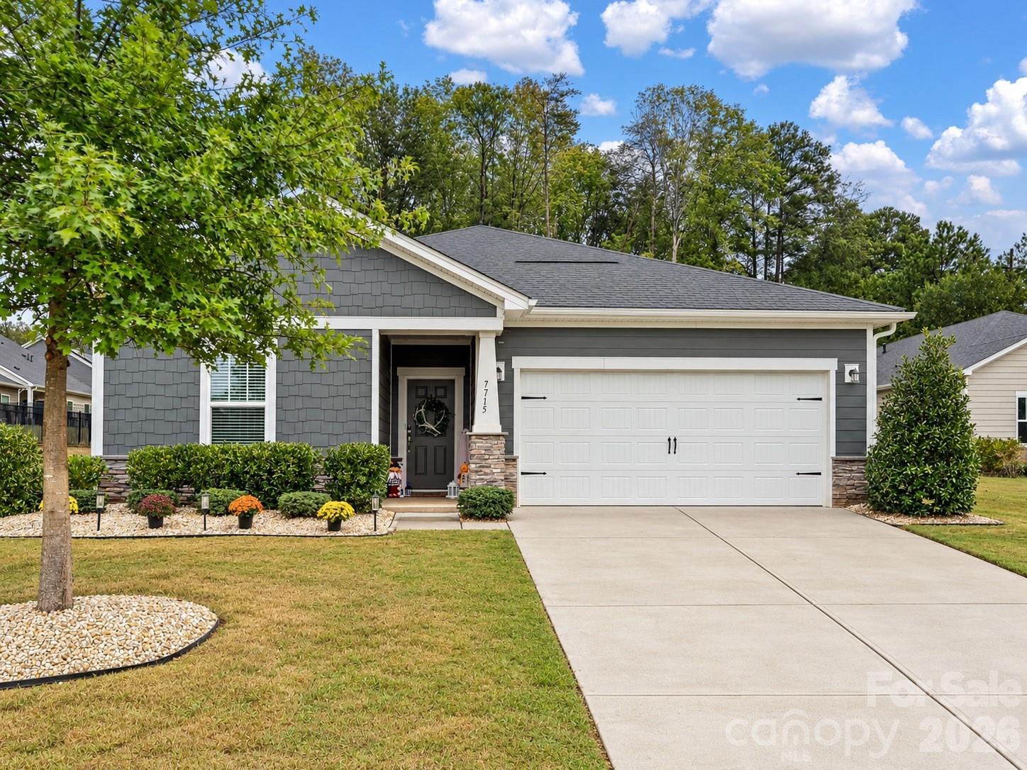 Gray-shingled home with white double garage, stone accents, and landscaped front yard.