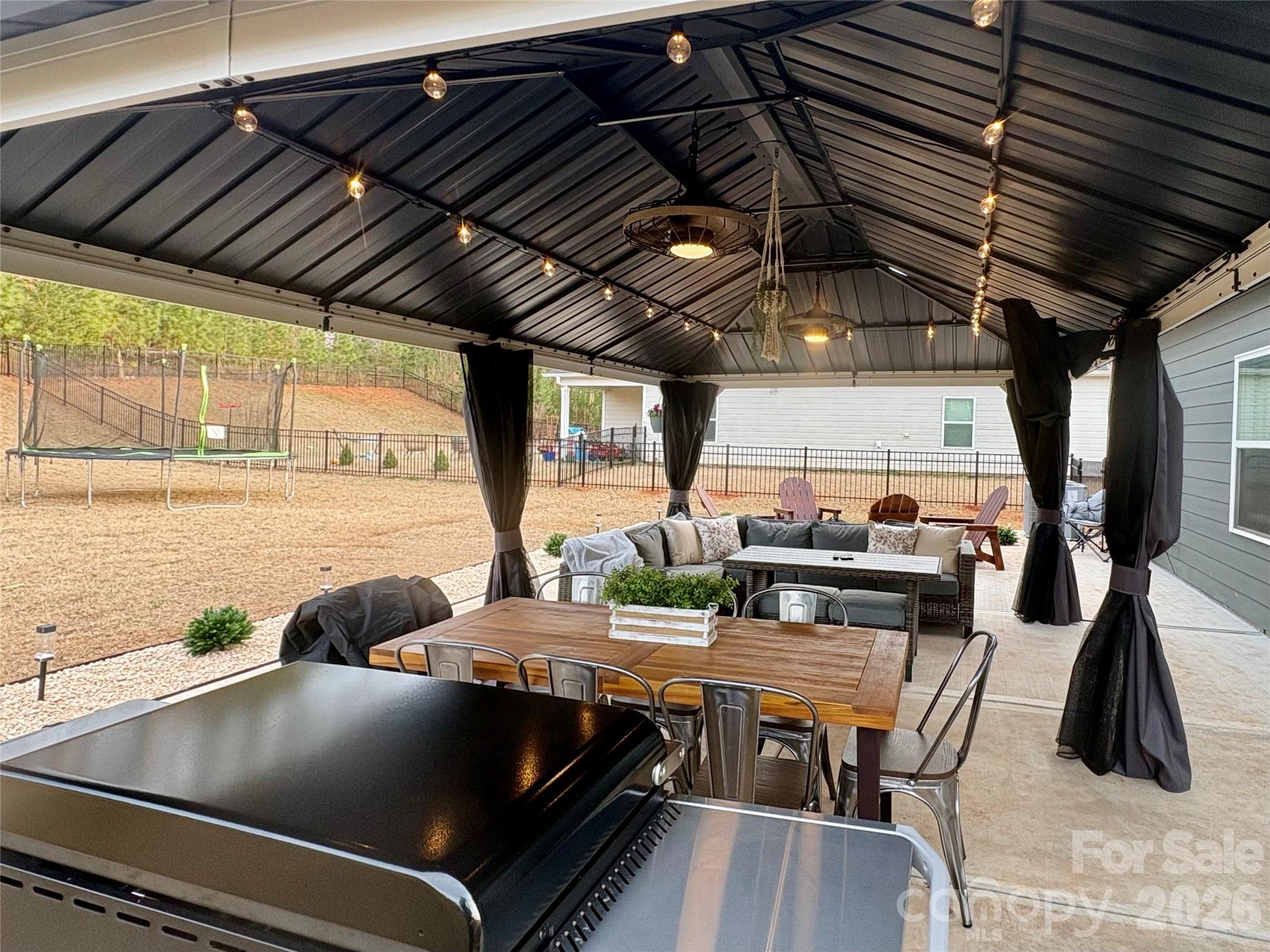 Covered patio with string lights, outdoor dining set, lounge seating, and a large grill.