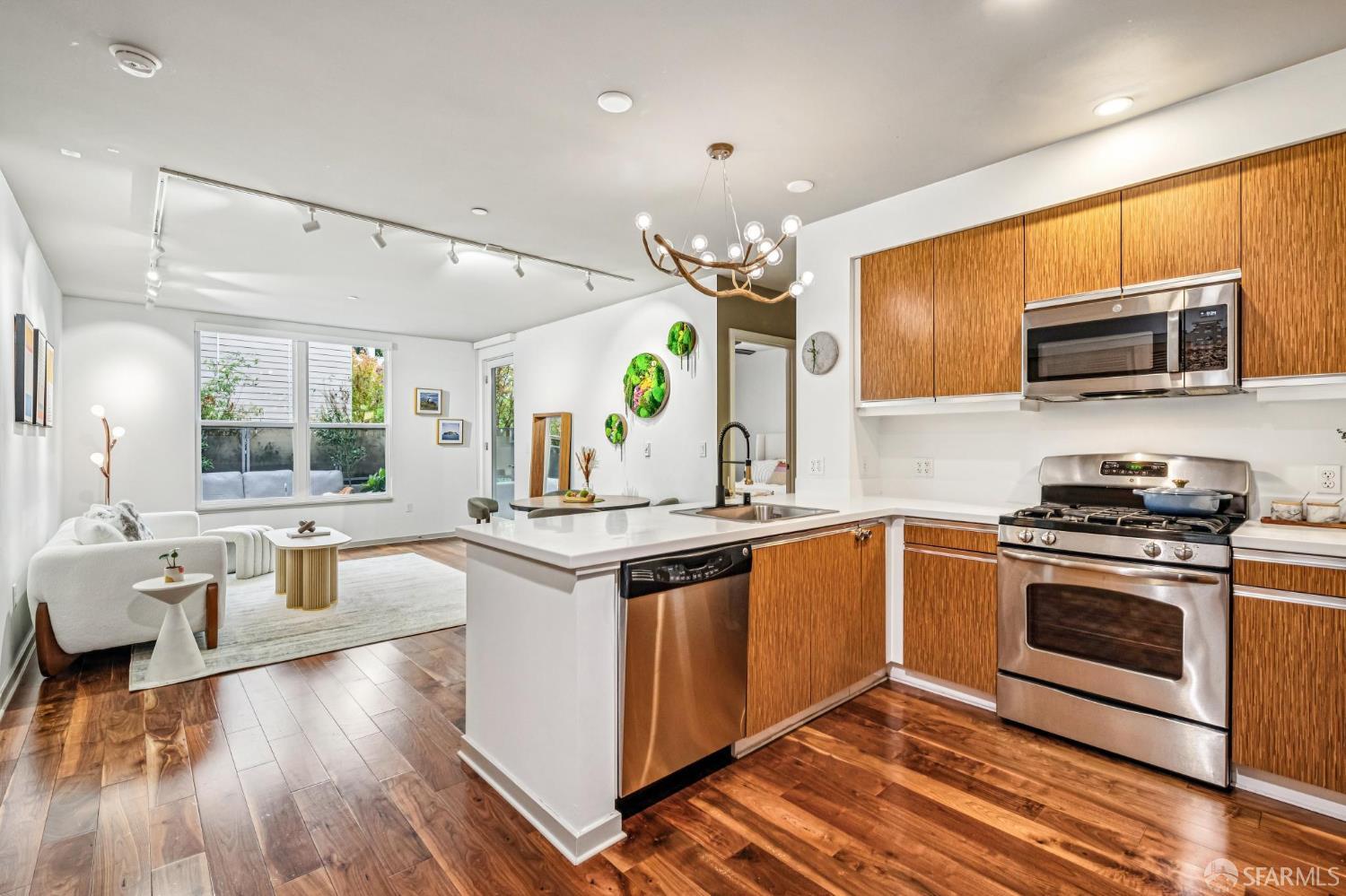 Open-plan kitchen with wood cabinetry and a white island beside a furnished living area.