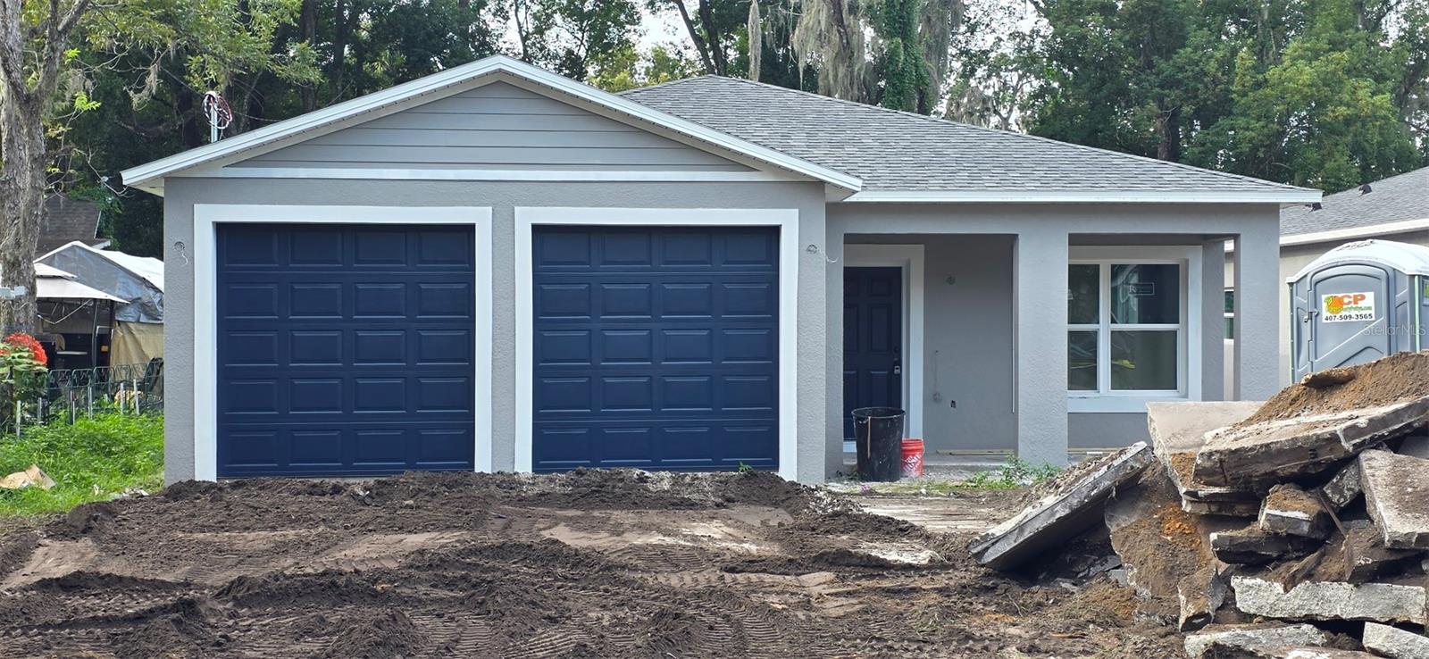 Gray house with twin navy garage doors and an unfinished, debris-strewn driveway.