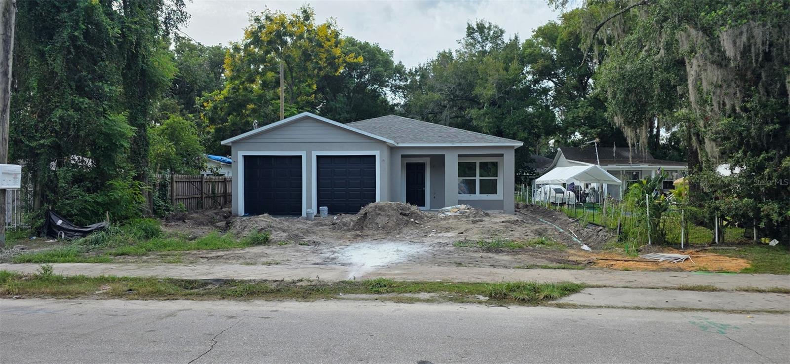 Gray house with two black garage doors and an unfinished, dirt-covered front yard.