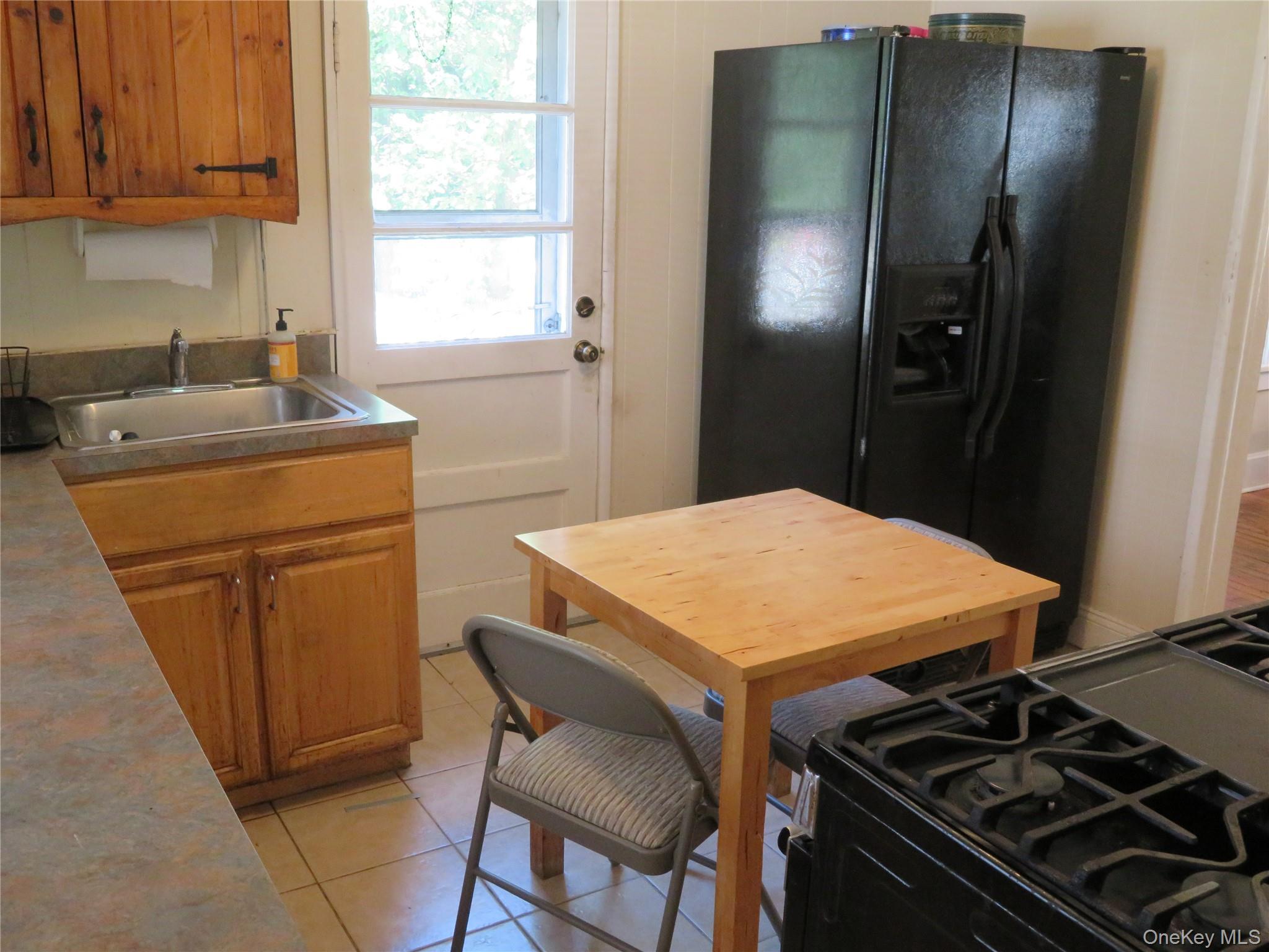 Kitchen with wooden cabinets, a black refrigerator, and a small wooden dining table.