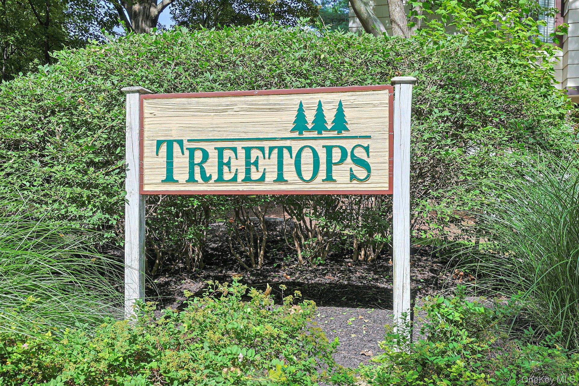 Treetops neighborhood sign with three evergreen tree symbols, surrounded by shrubs and grasses.