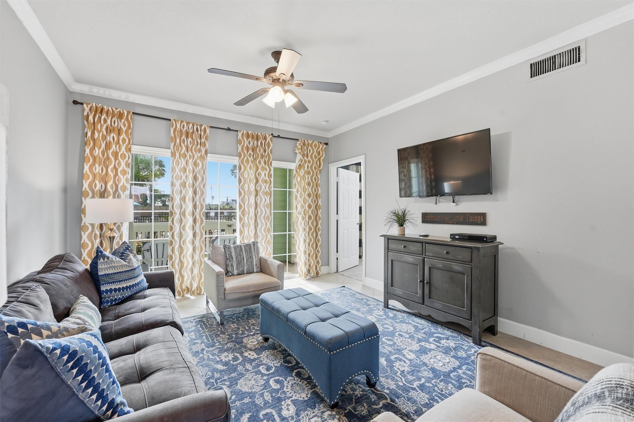 Living room with gray sofas, blue ottoman, patterned rug, and gold-and-white curtains.