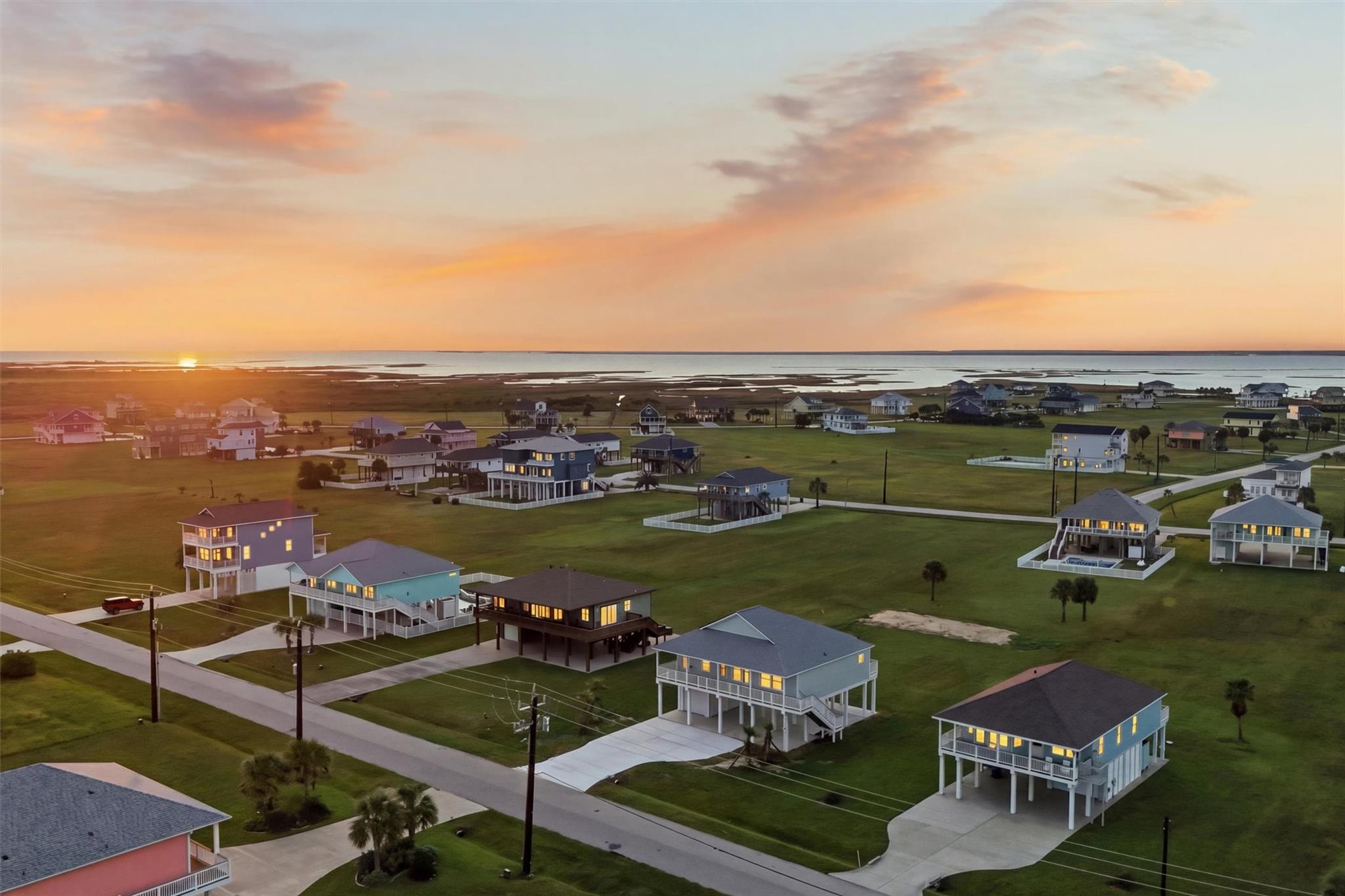 Aerial view of coastal homes beside tidal water at sunset.
