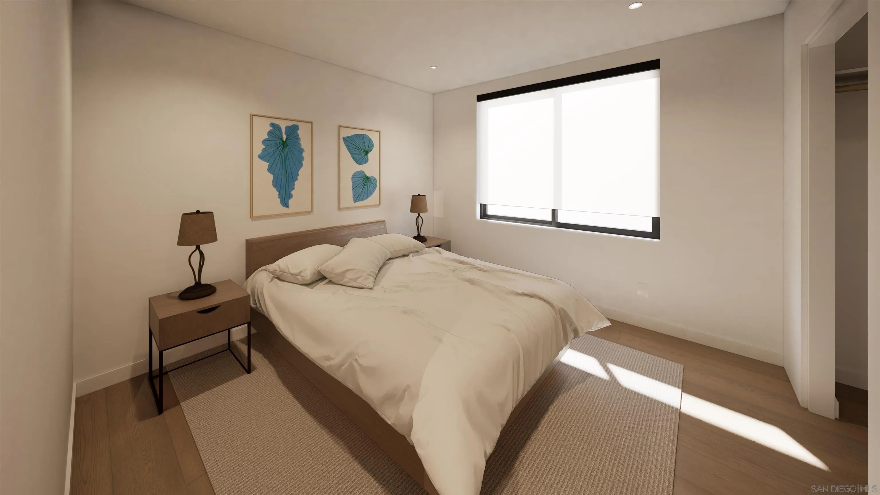 Furnished bedroom with white bedding, blue botanical prints, and sunlight falling across a neutral rug.