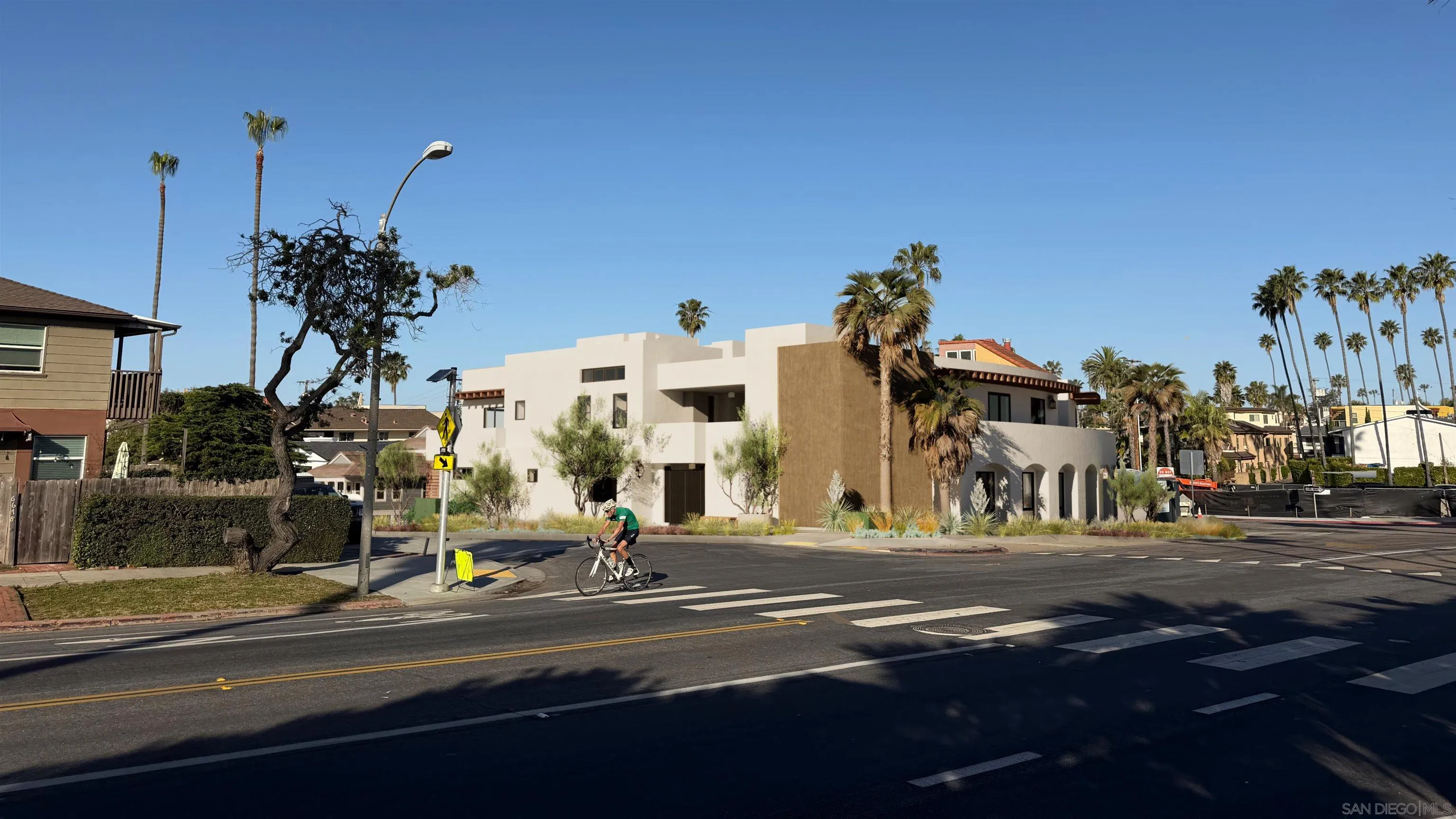 Modern white and tan building with arched openings and palm trees beside a street intersection.