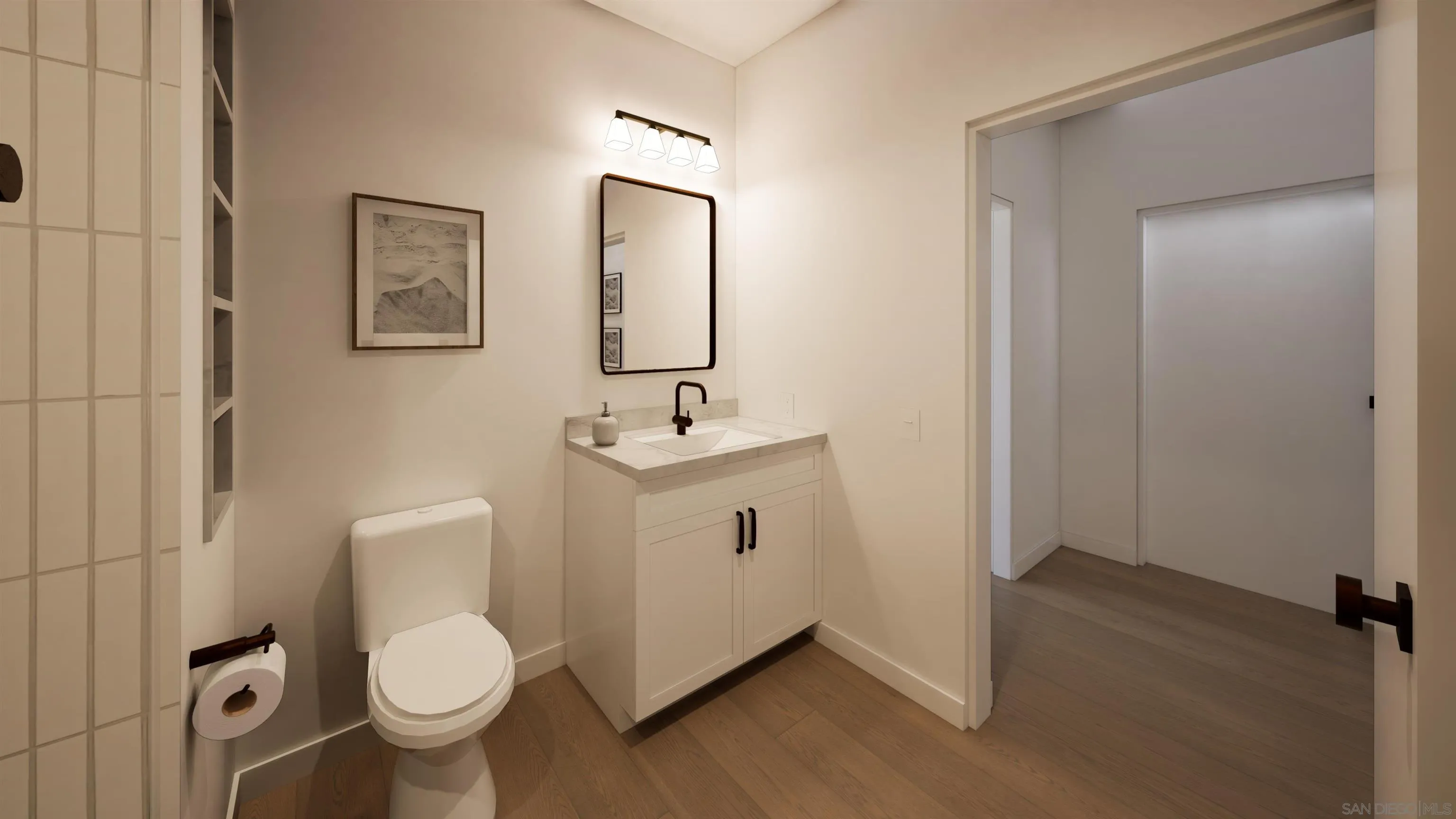 Bathroom with a white vanity and black faucet, toilet, framed art, and an open doorway to a wood-floored room.