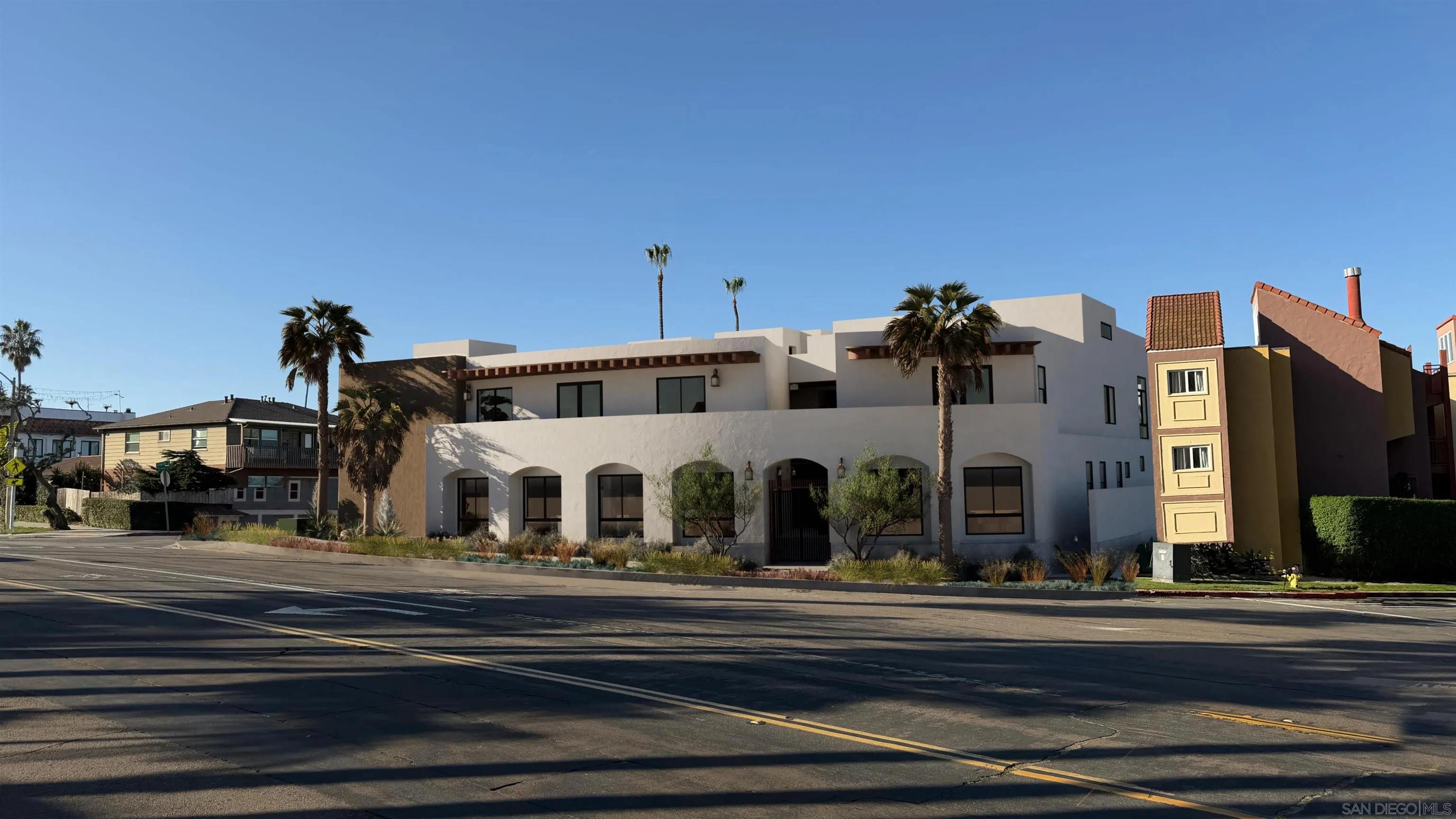 Modern white stucco residential building with arched windows, landscaped frontage, and palm trees.