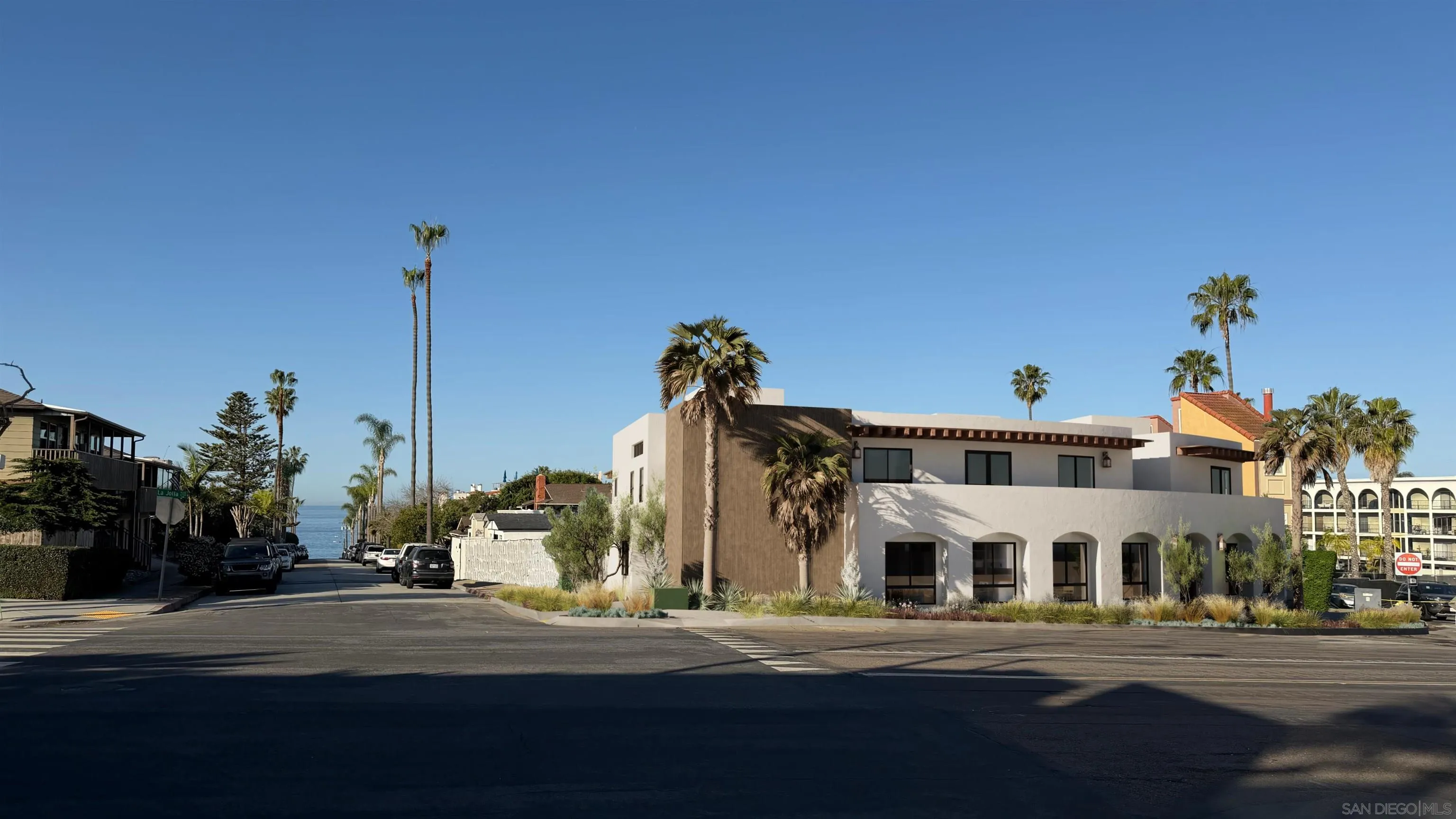Modern La Jolla building at a palm-lined street corner, with the ocean visible down the road.
