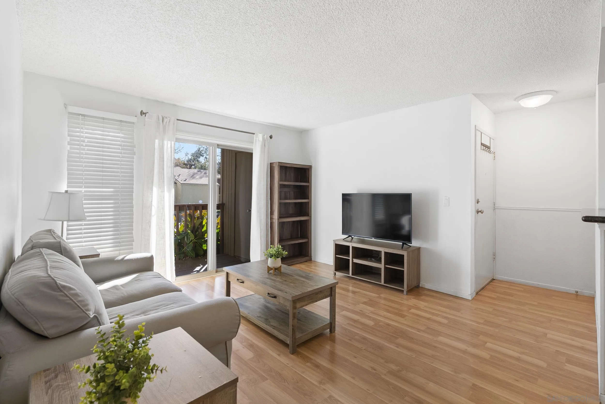 Living room with a gray sectional, wood furnishings, and a sliding door to a balcony.