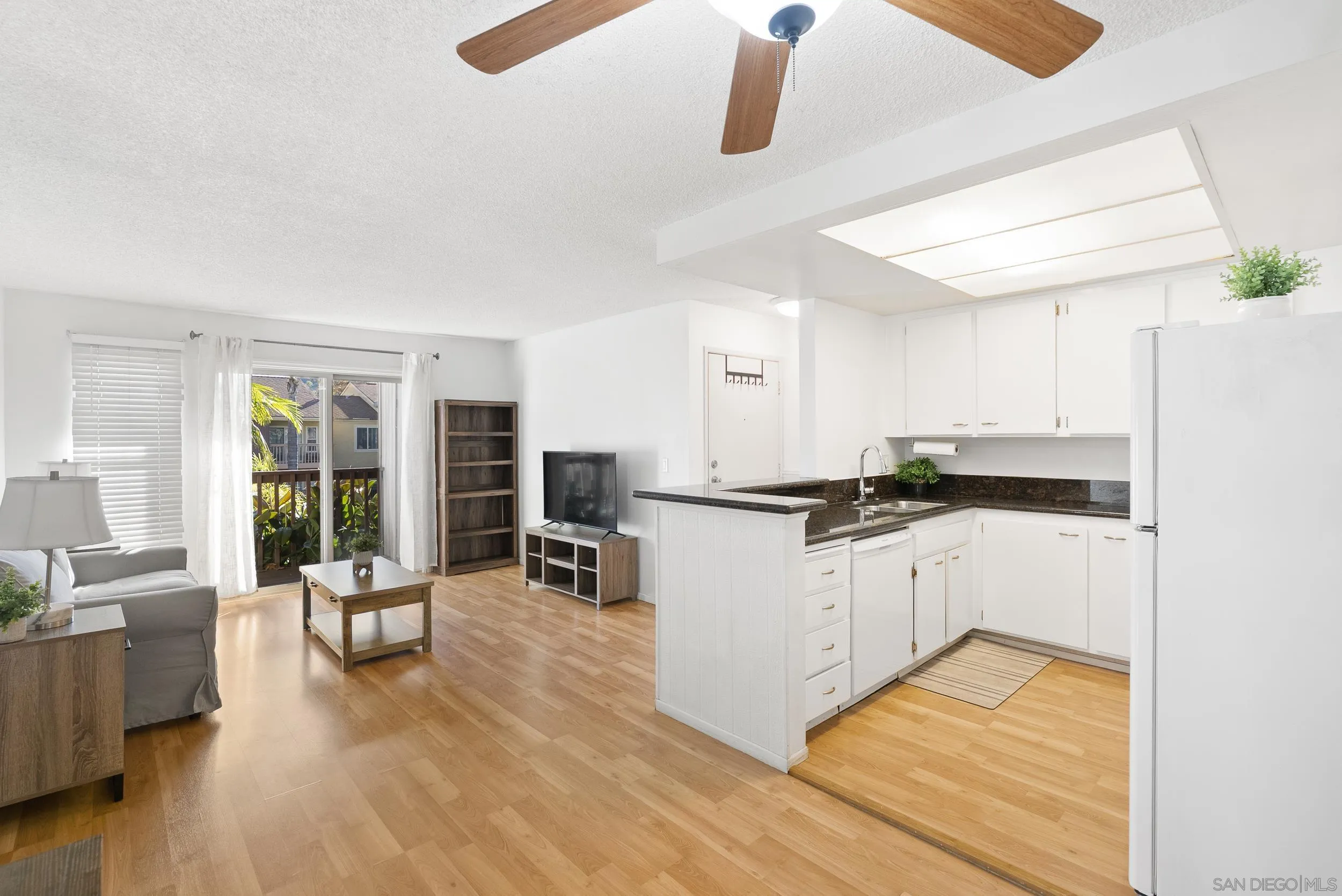 Open-plan living room and kitchen with white cabinets, wood floors, and sliding doors to a balcony.