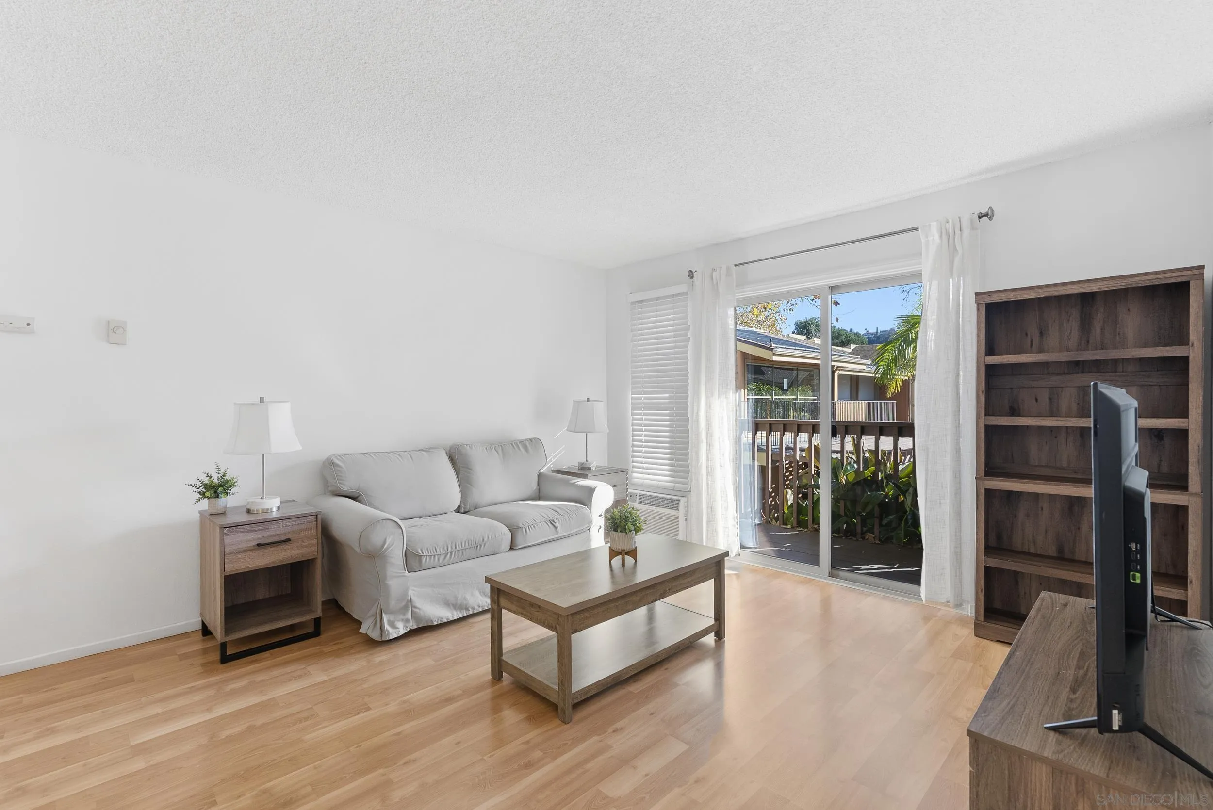 Furnished living room with a white sofa and sliding doors opening to a plant-lined balcony.