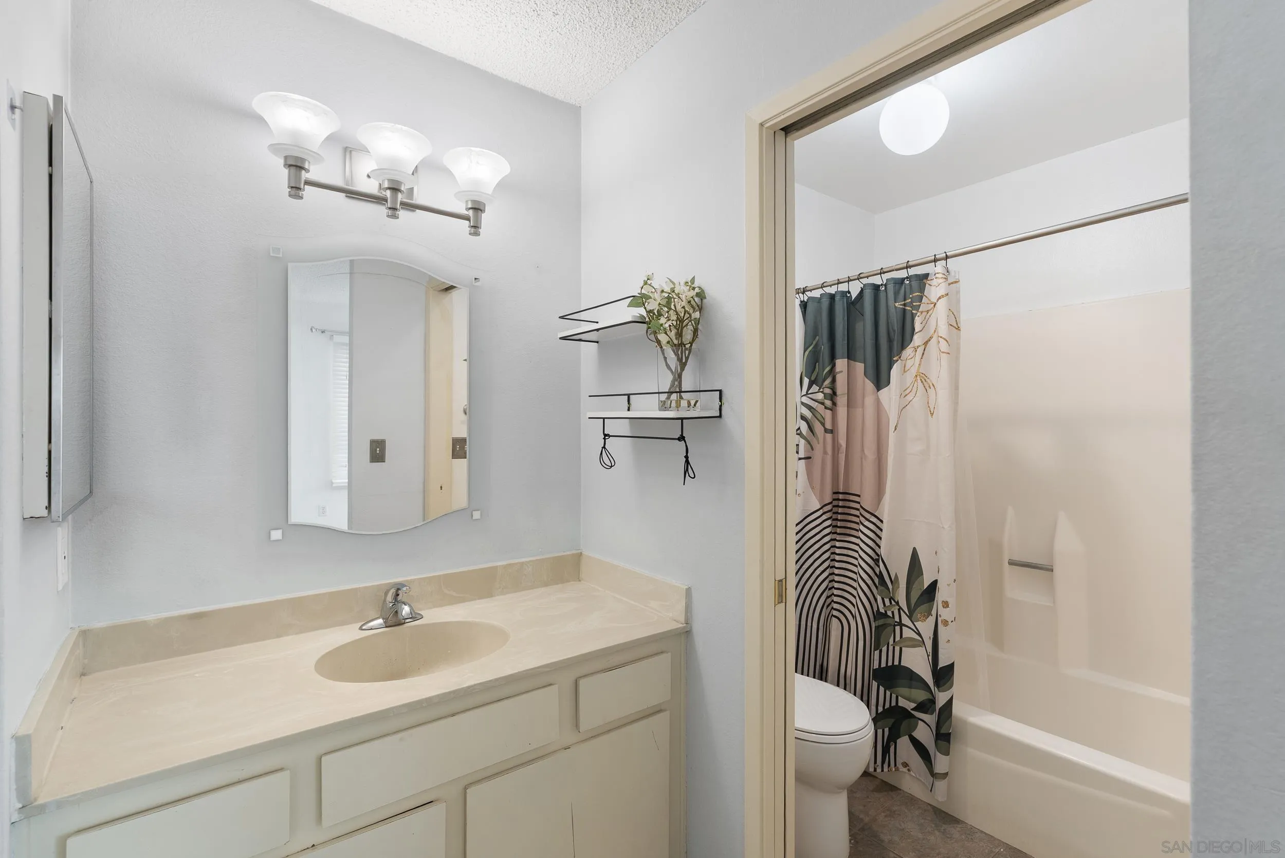 Bathroom with a beige vanity and sink beside a bathtub and patterned shower curtain.