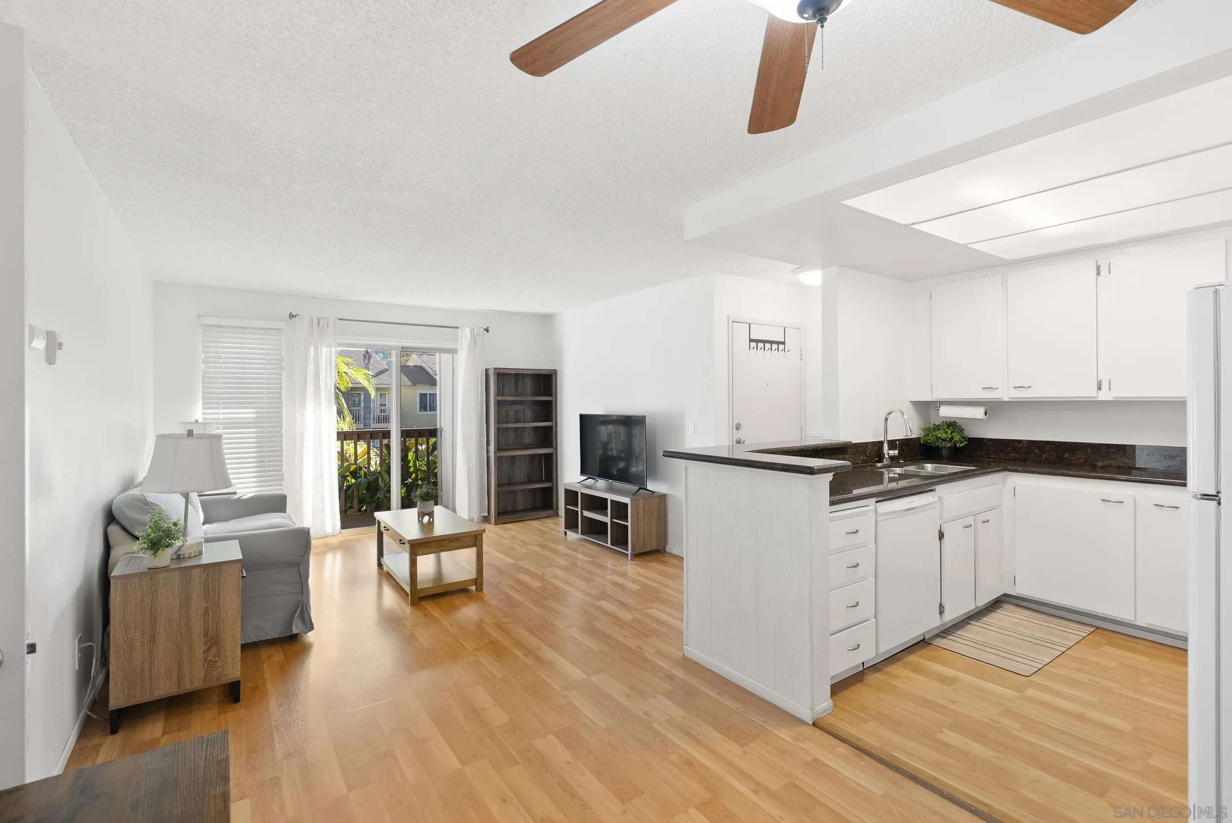 Open-plan condo living room and kitchen with white cabinets, wood floors, and a balcony slider.