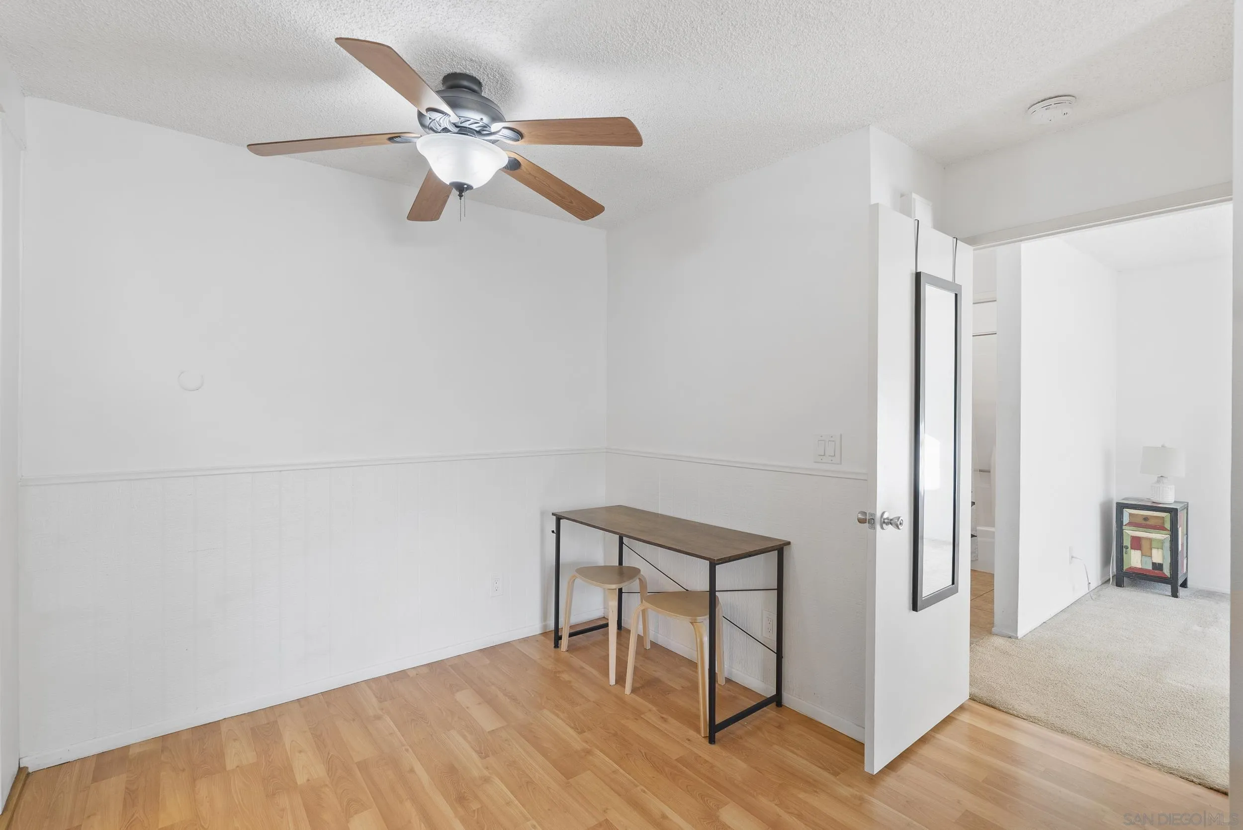 Bright room with a ceiling fan, wood flooring, and a narrow table with two stools.