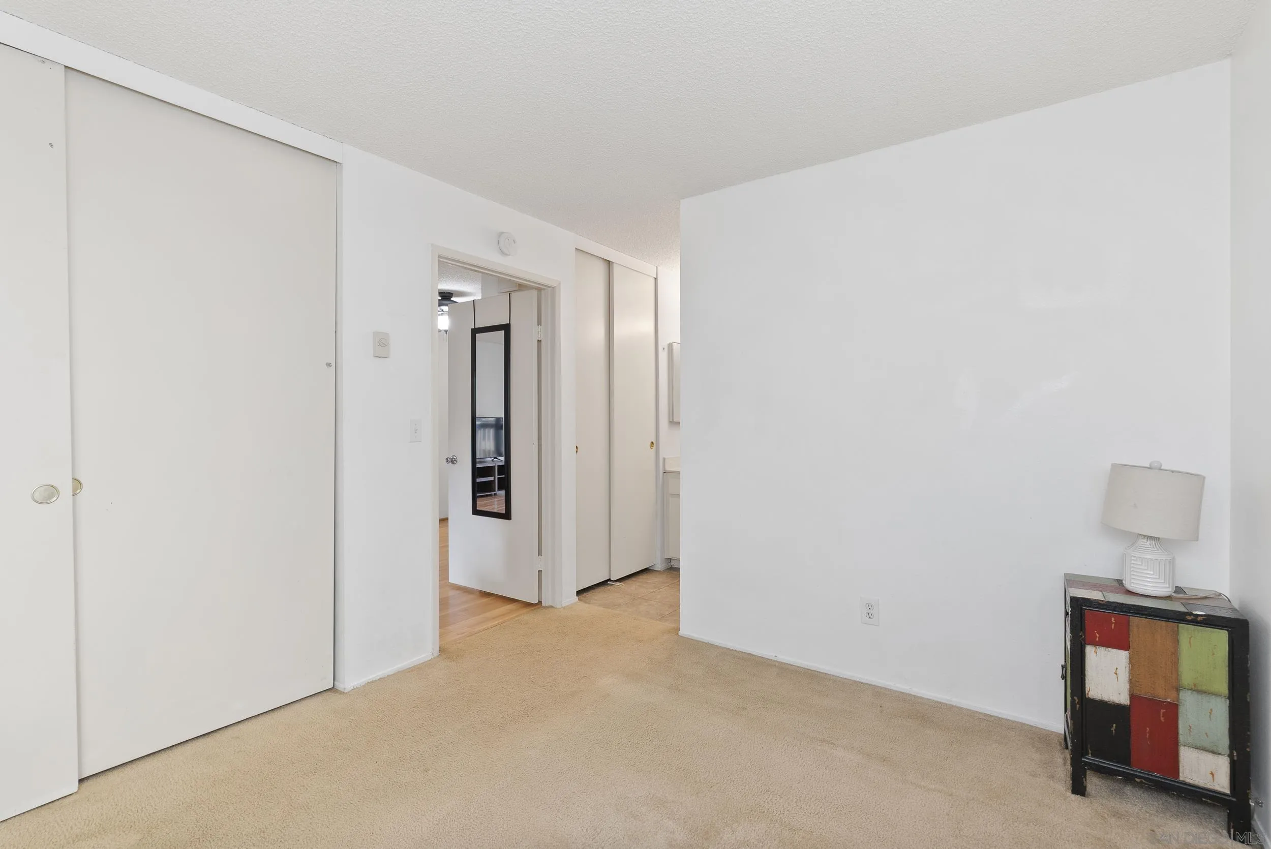 Carpeted room with sliding closet doors and a colorful cabinet topped with a lamp.