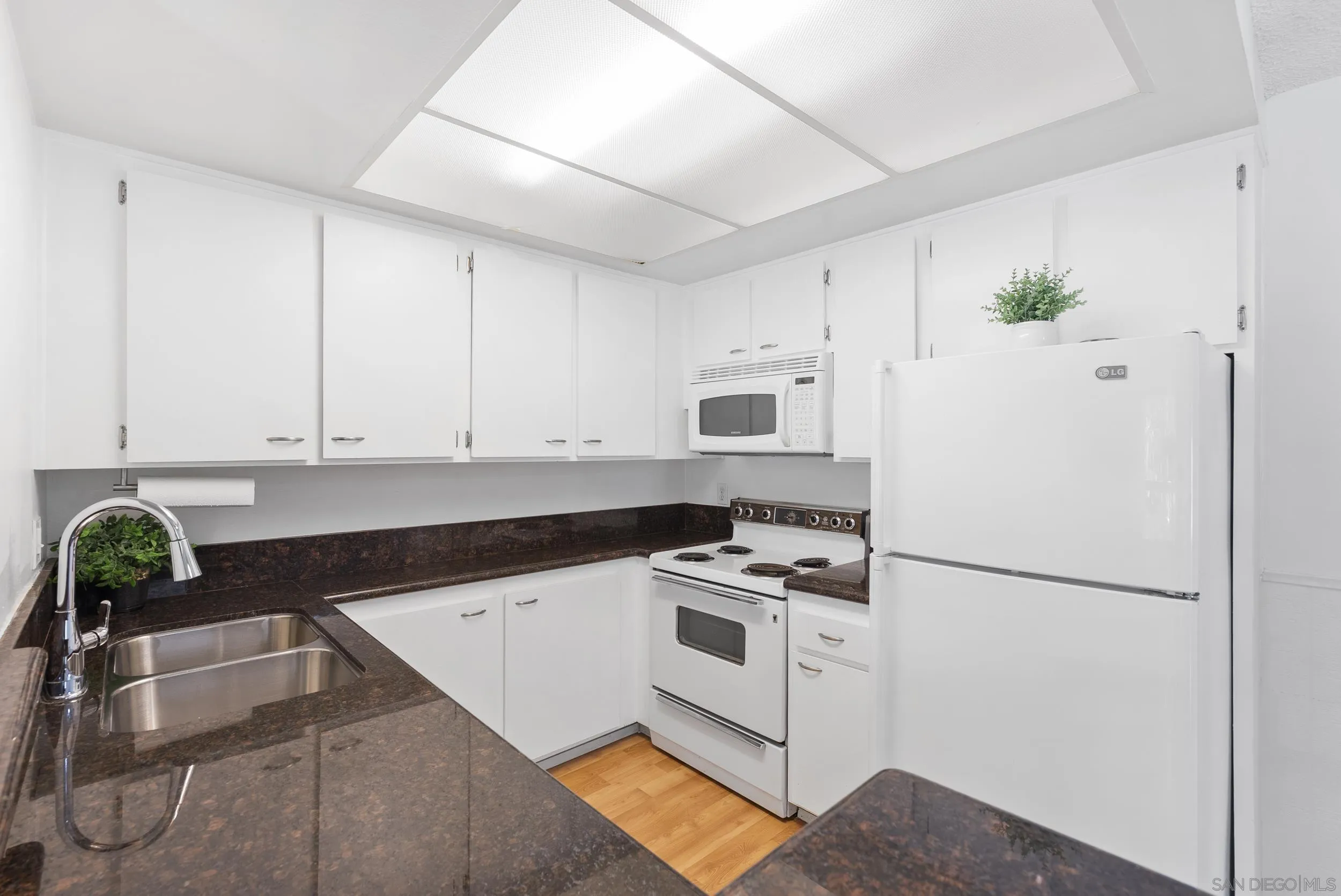 Kitchen with white cabinets and appliances, dark granite counters, and a double-basin sink.