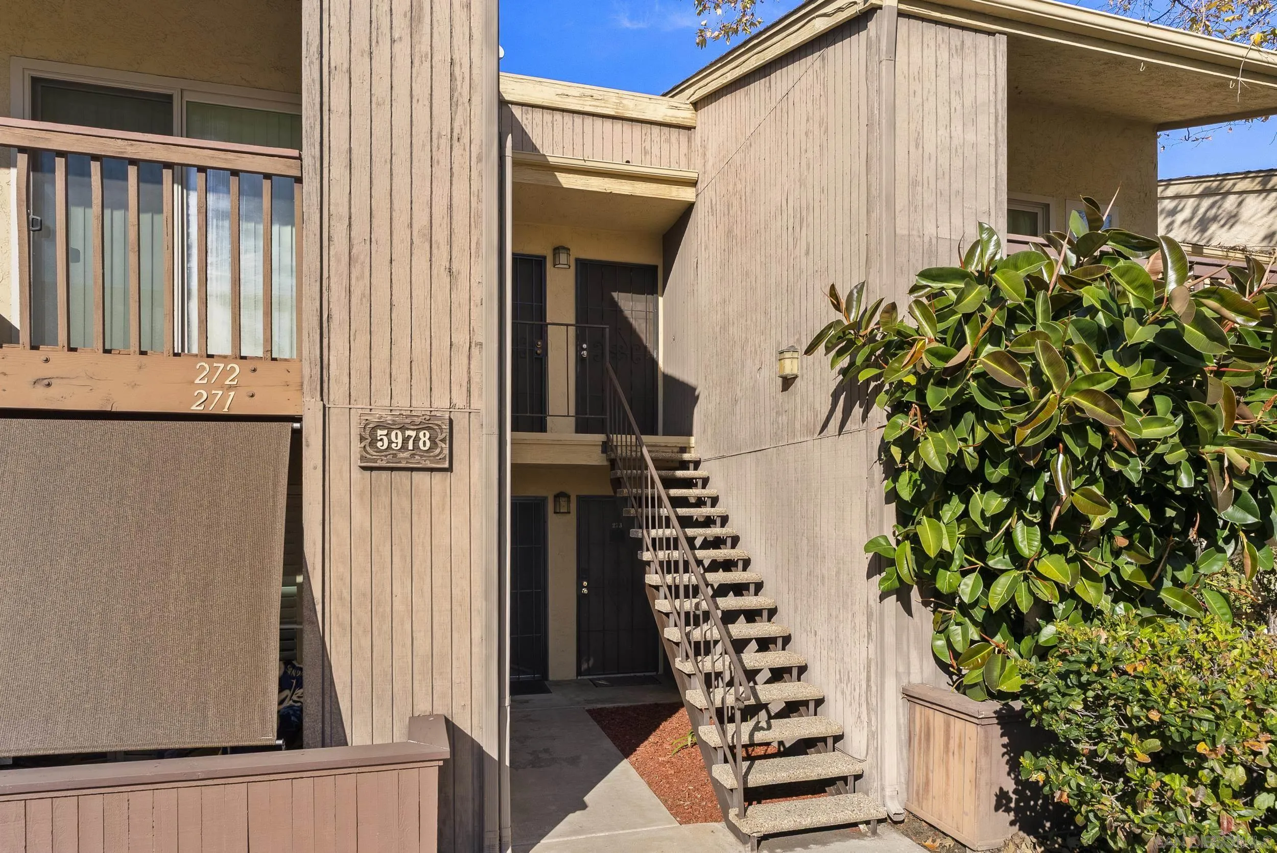 Condominium entrance with an outdoor staircase, wood siding, and a large leafy shrub.