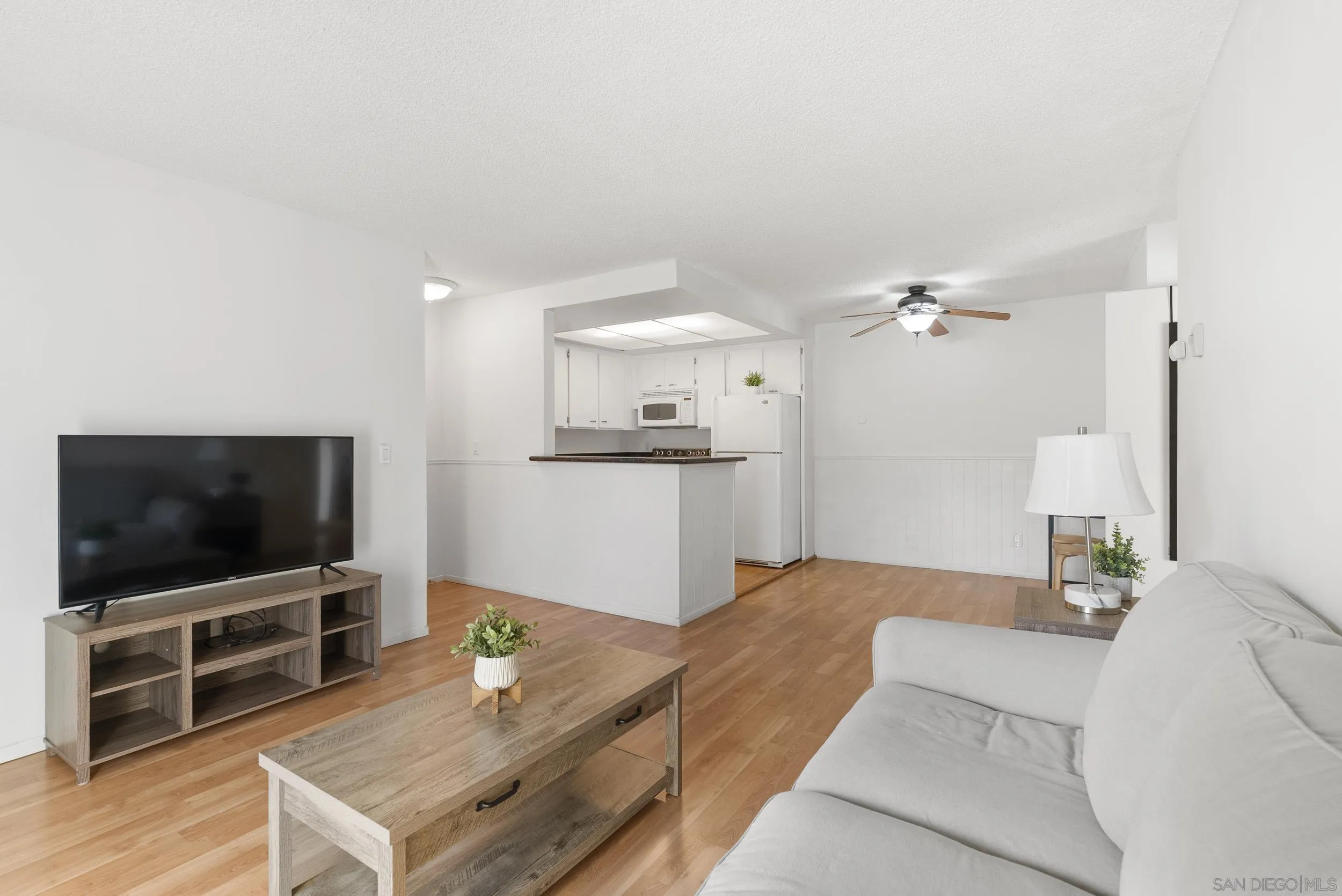 Living room with a white sofa and wood floors, opening to a compact kitchen with a breakfast bar.