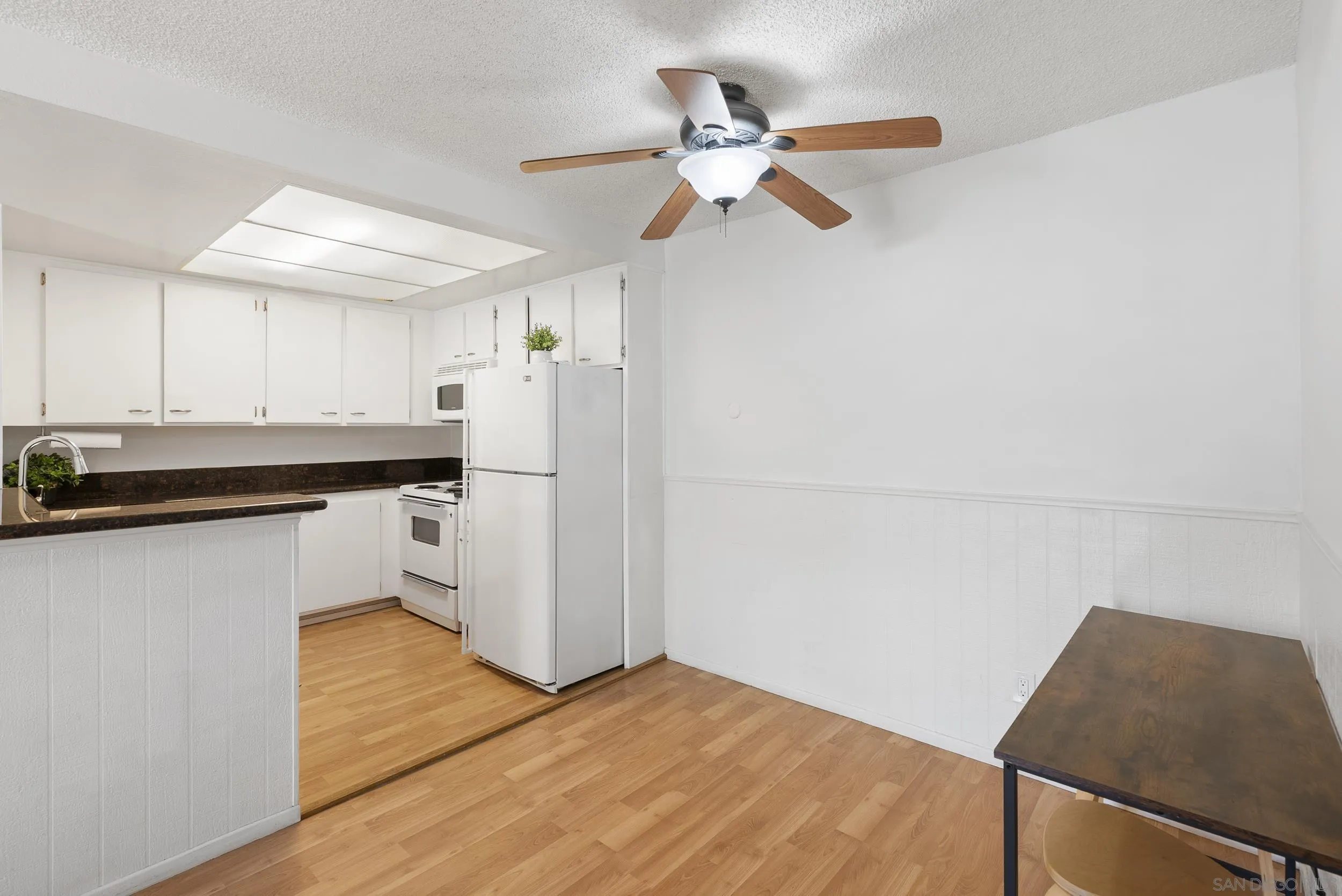 Kitchen and dining area with white appliances, wood flooring, and a dark table.