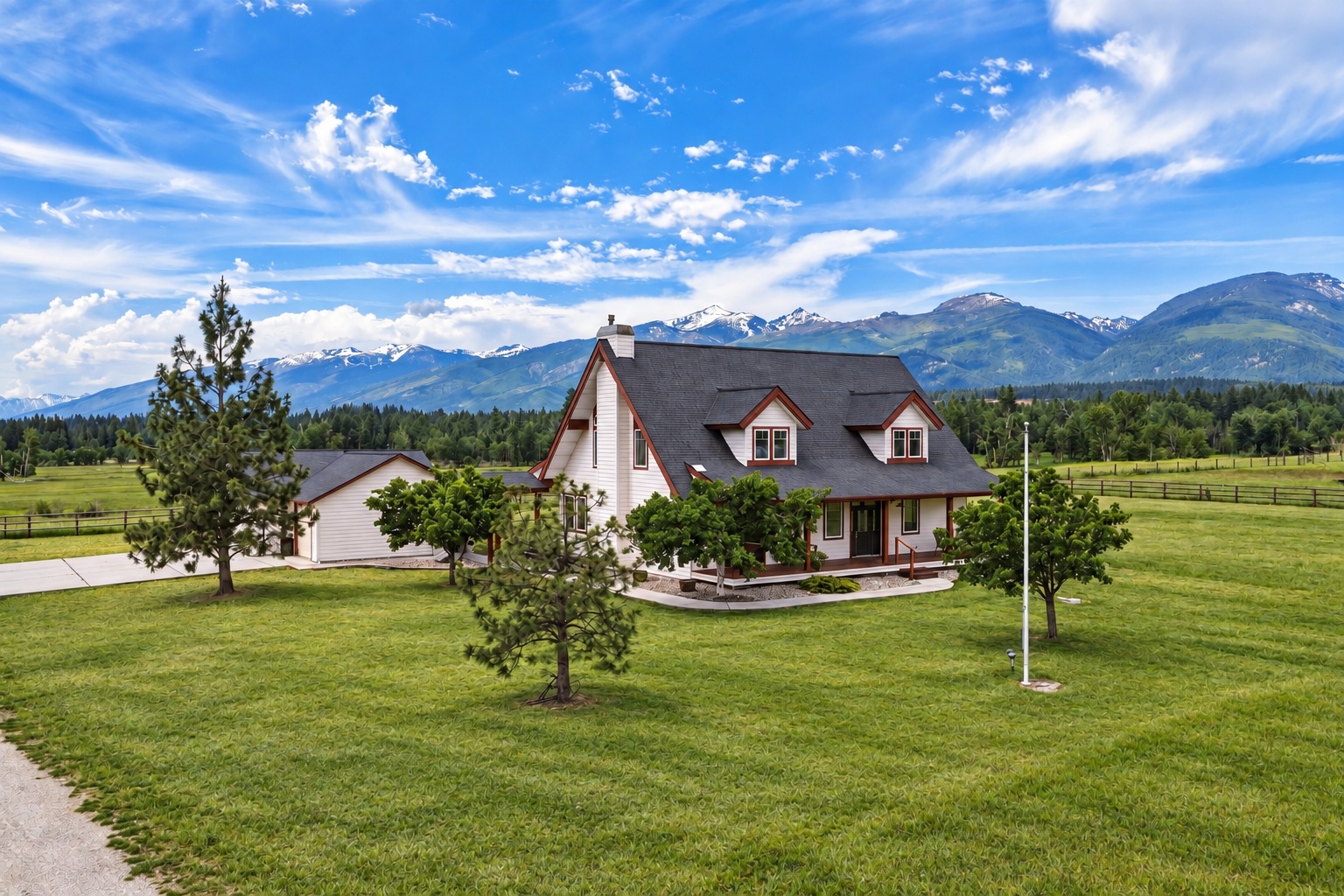 White two-story house with red trim on a broad lawn, backed by snow-capped mountains.