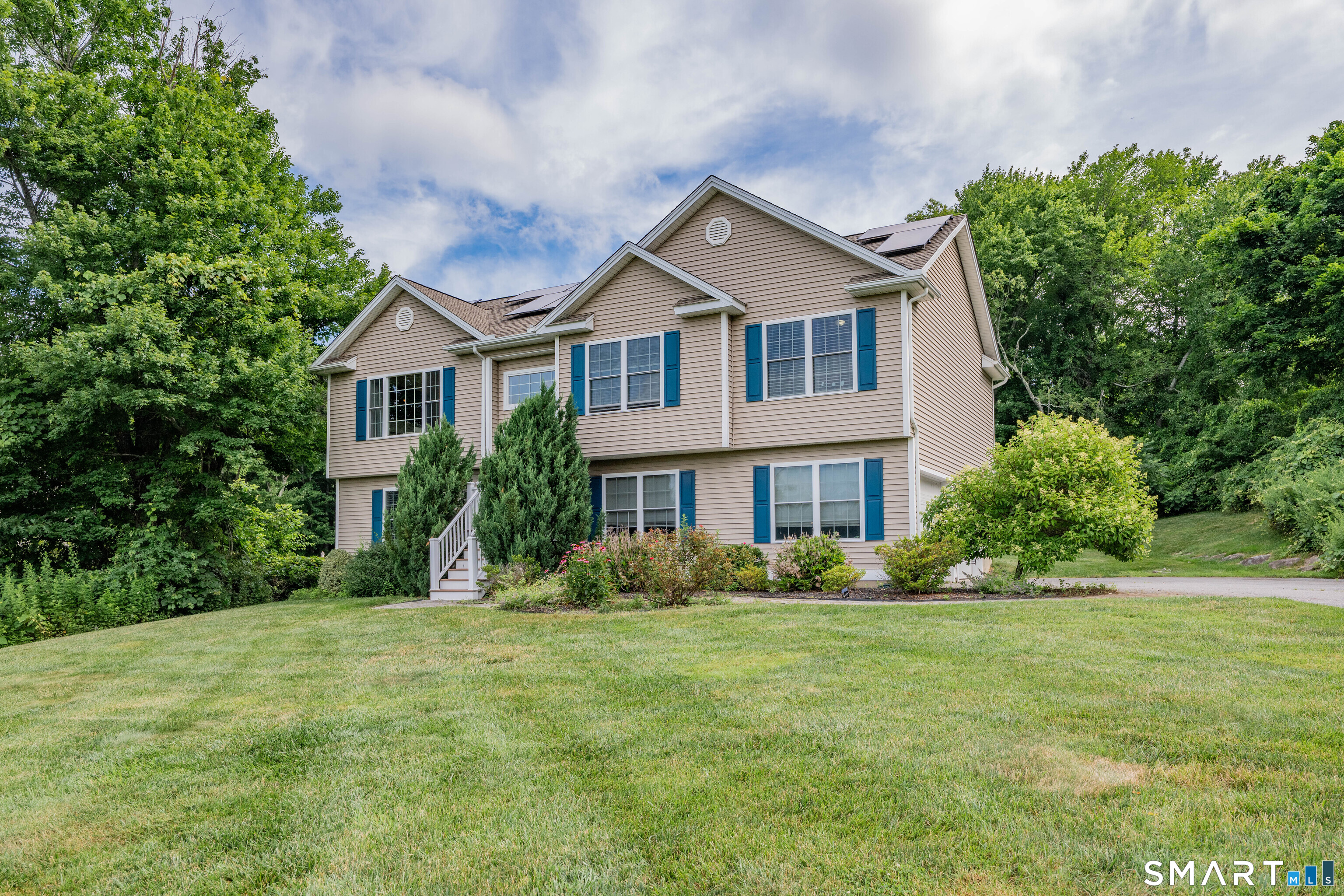 Two-story beige house with blue shutters, rooftop solar panels, and a landscaped lawn.