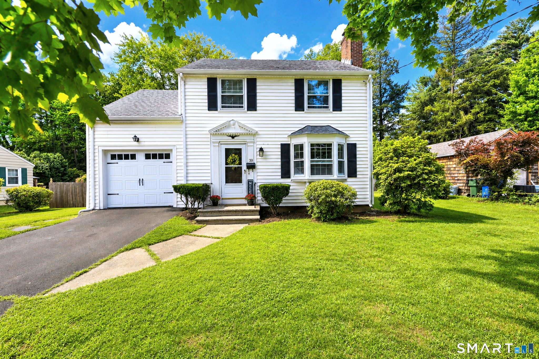 White two-story house with black shutters, an attached garage, and a bay window.
