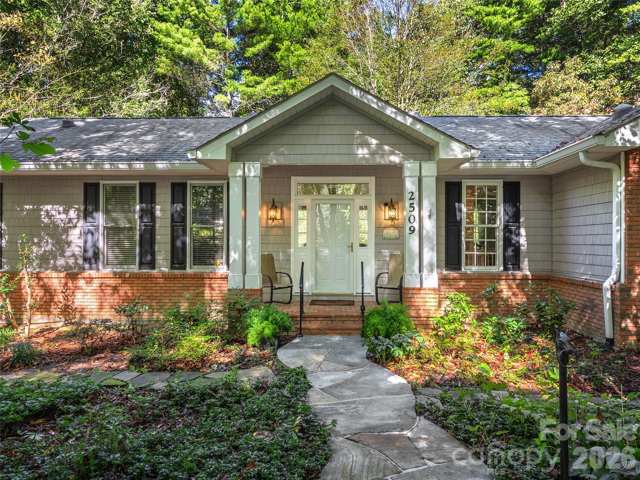 Single-story home with a covered entry, brick foundation, and curved stone walkway through landscaped gardens.