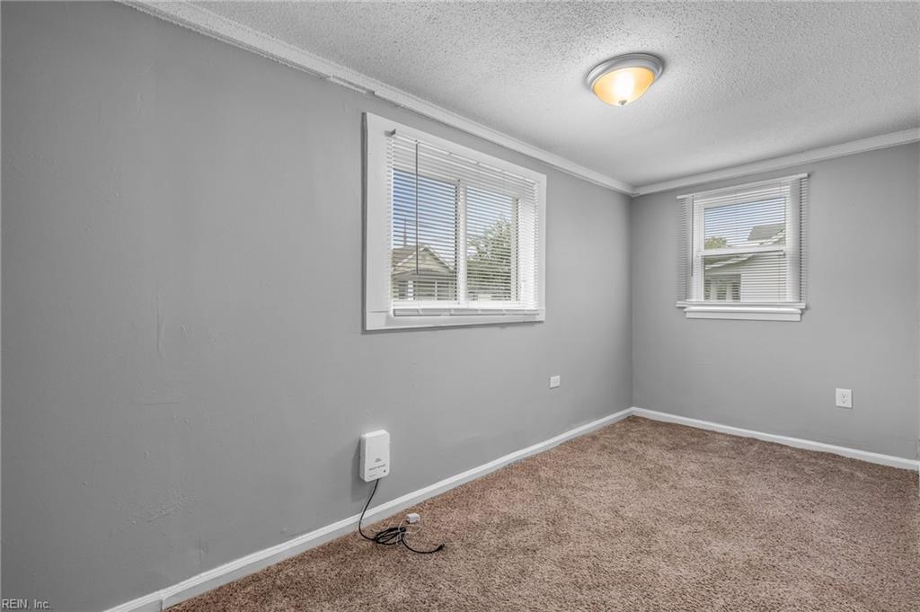 Empty carpeted room with gray walls, two windows with blinds, and a wall-mounted heater.