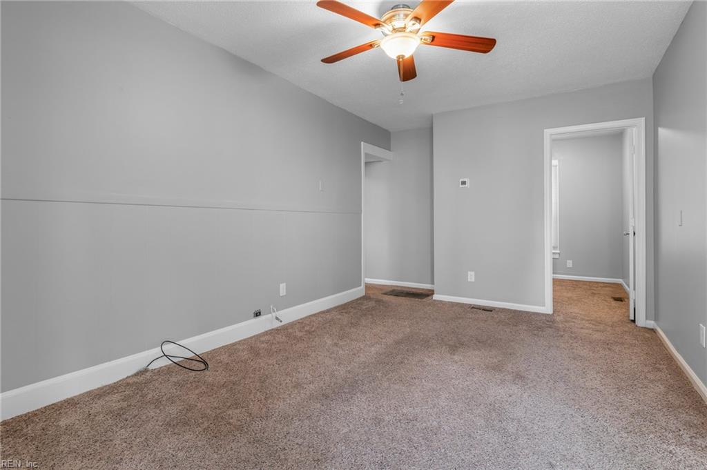 Empty carpeted room with gray walls, a wood-blade ceiling fan, and open doorways.