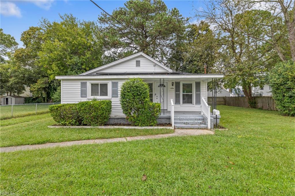 White single-story house with a covered porch, front steps, trimmed shrubs, and a broad lawn.