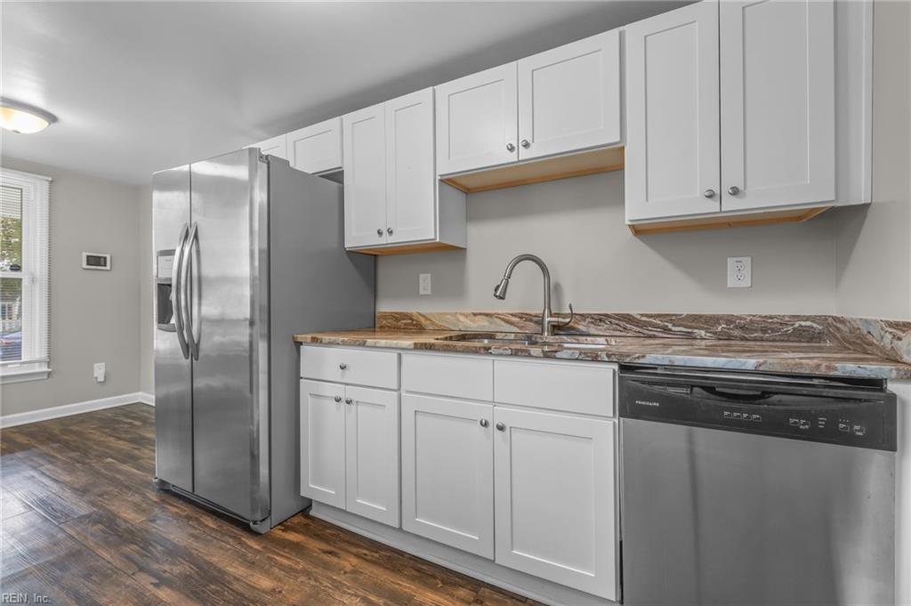 Kitchen with white cabinets, patterned stone counters, stainless appliances, and dark wood-look flooring.